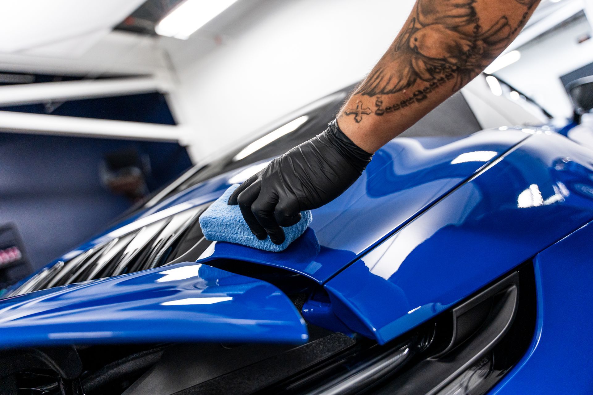 Person in black glove applying product to shiny blue car with a blue applicator.