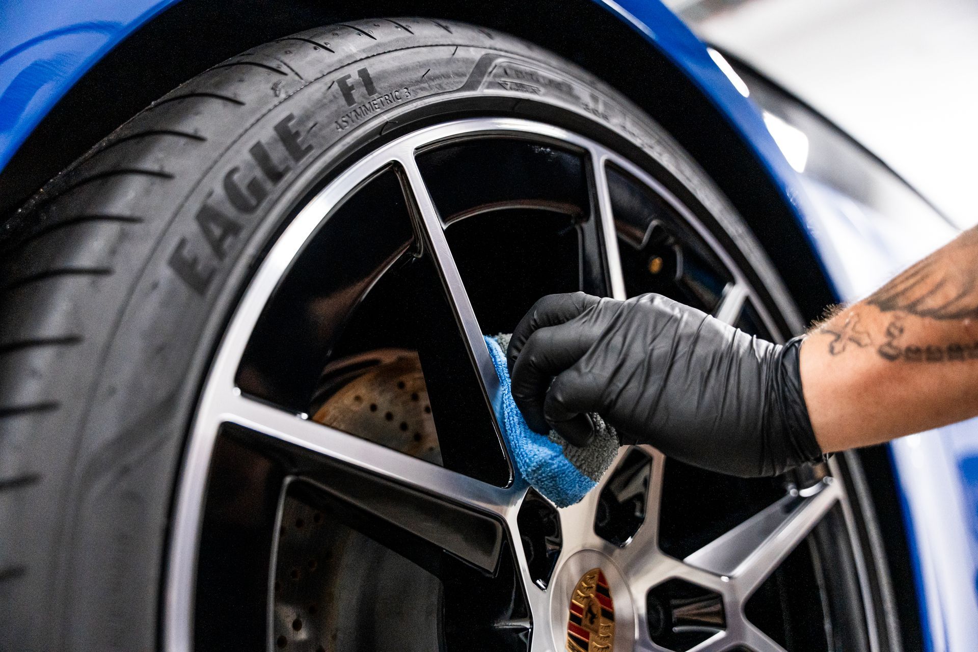 Person in black gloves applying detailing product to a car's wheel, blue car, black and silver wheel.