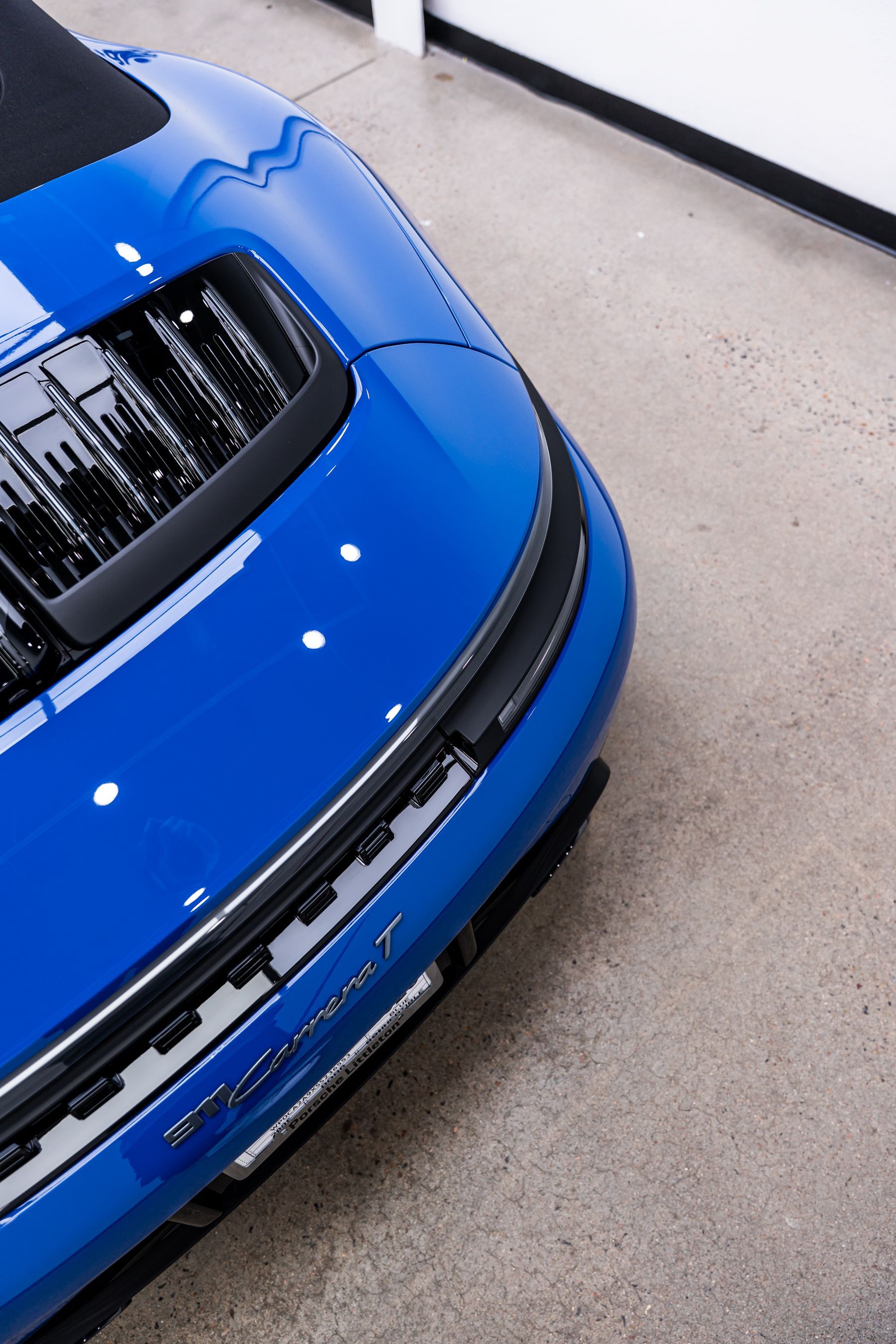 Blue sports car, close-up of front end with hood scoop and white racing stripes, on a concrete floor.