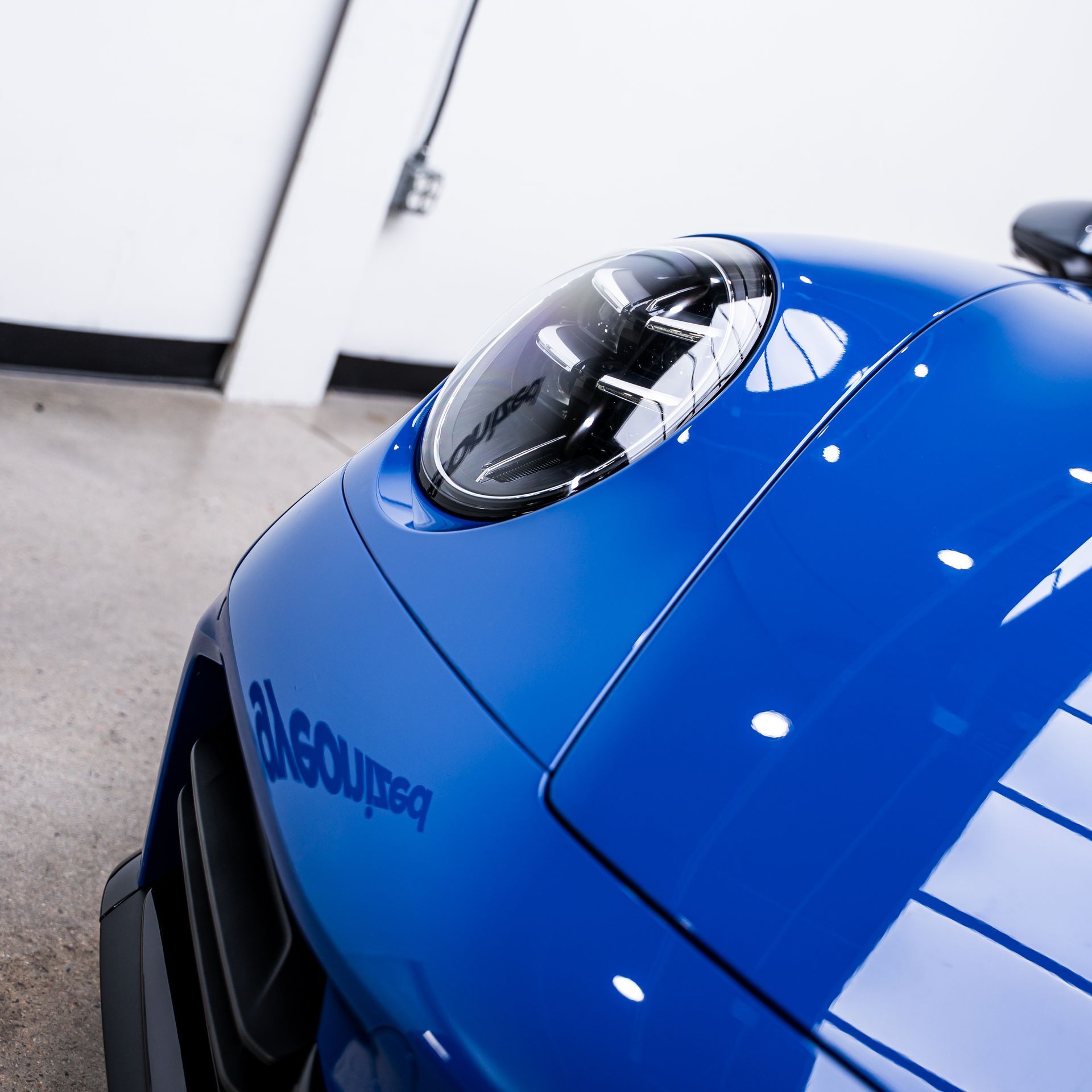Blue sports car, close-up view of the hood and headlight, indoors.