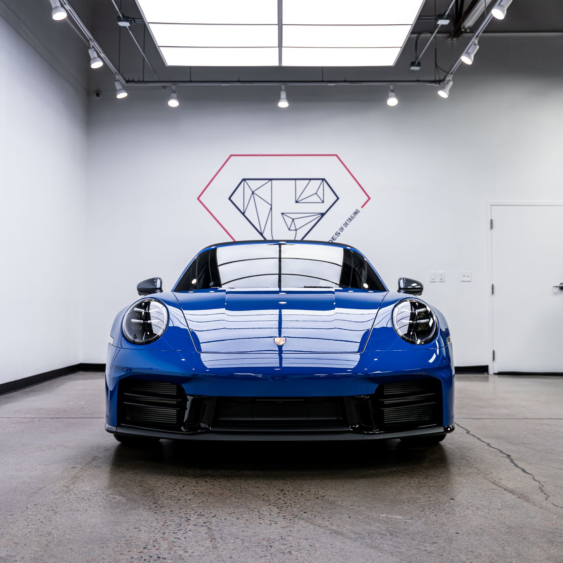 Blue Porsche 911 in a white showroom with logo on the wall.