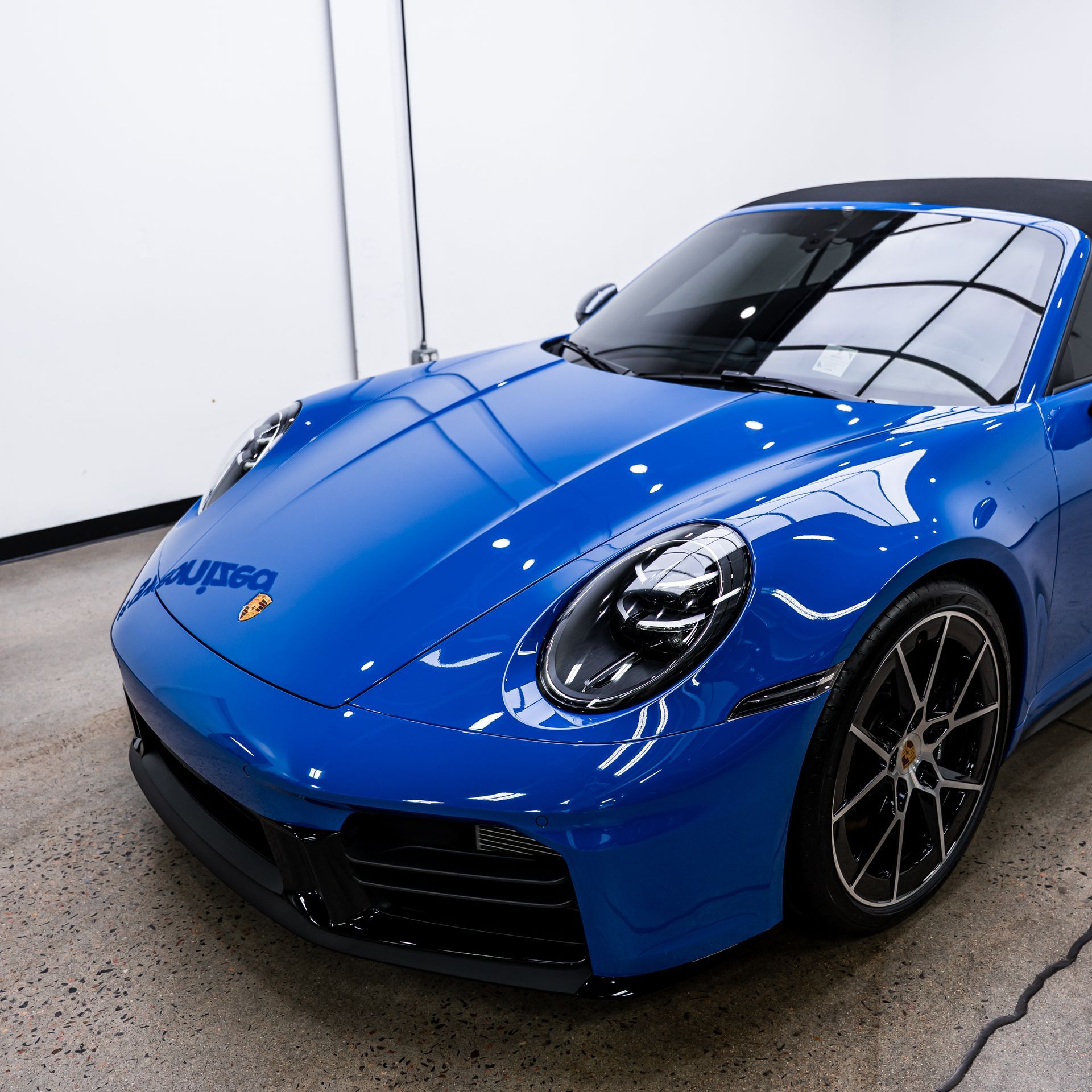Blue Porsche convertible parked indoors on a concrete floor.