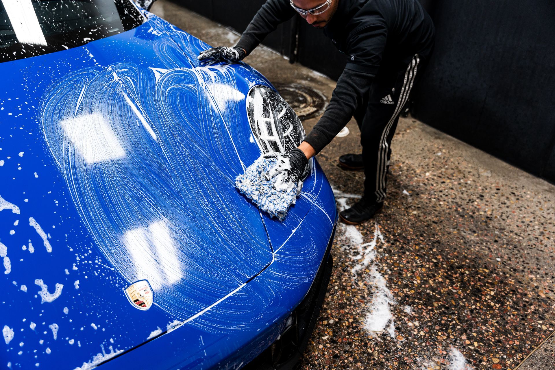 Person washing a blue car with soapy water, outdoors.