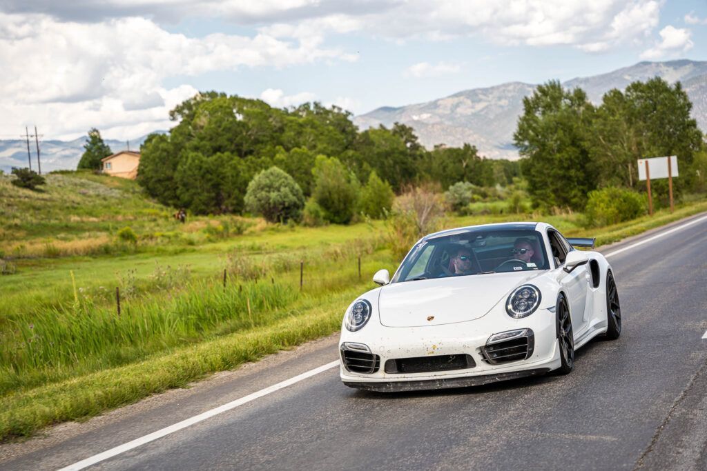 A white porsche turbo is driving down a country road.