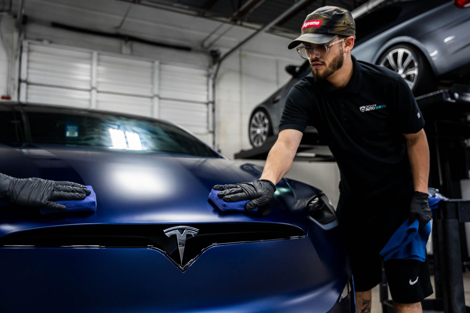 A man is cleaning the hood of a tesla model s in a garage.