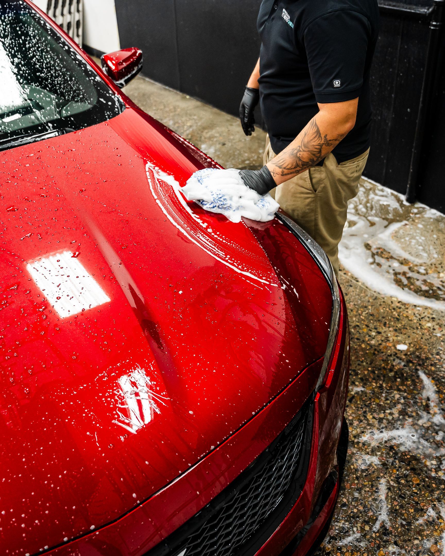 A man is washing a red car with a sponge.