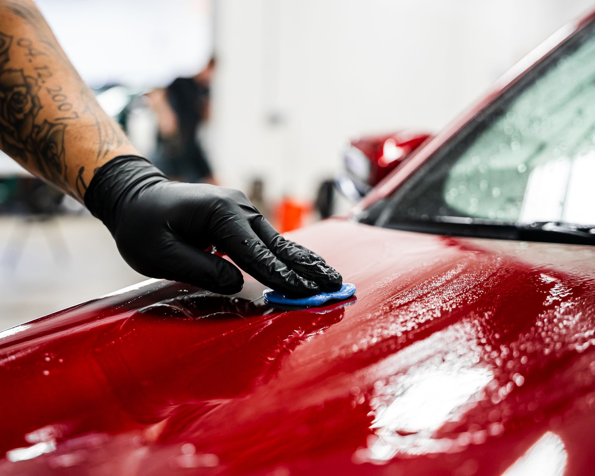 A person wearing black gloves is polishing the hood of a red car.