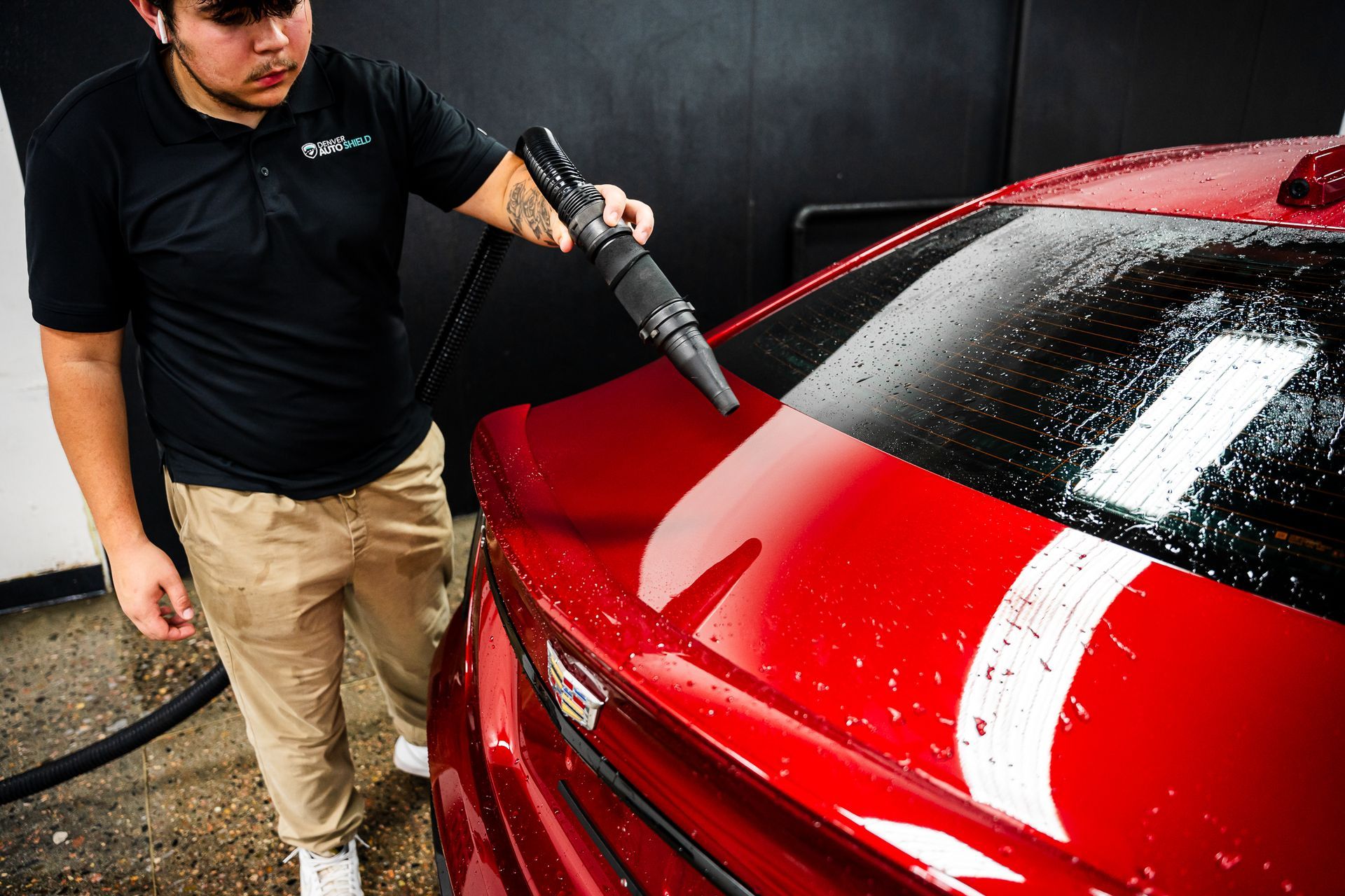 A man is cleaning a red car with a vacuum cleaner.