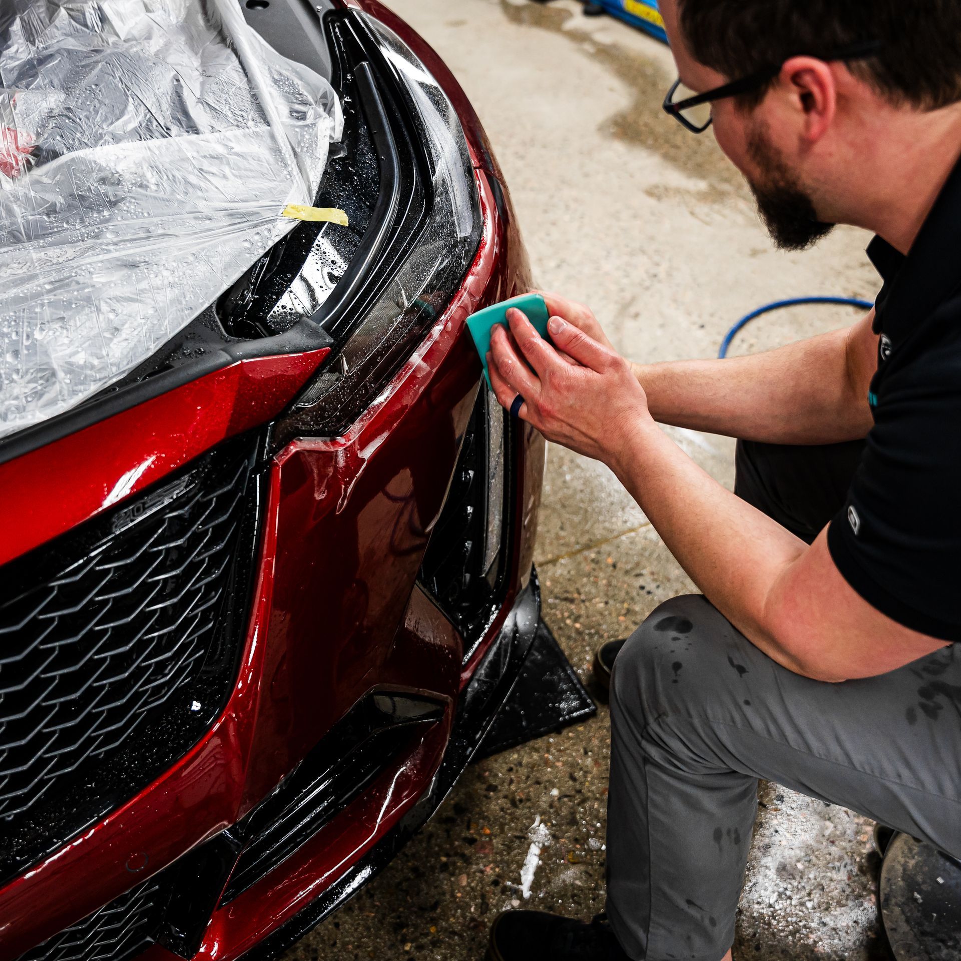 A man is cleaning the front of a red car with a sponge