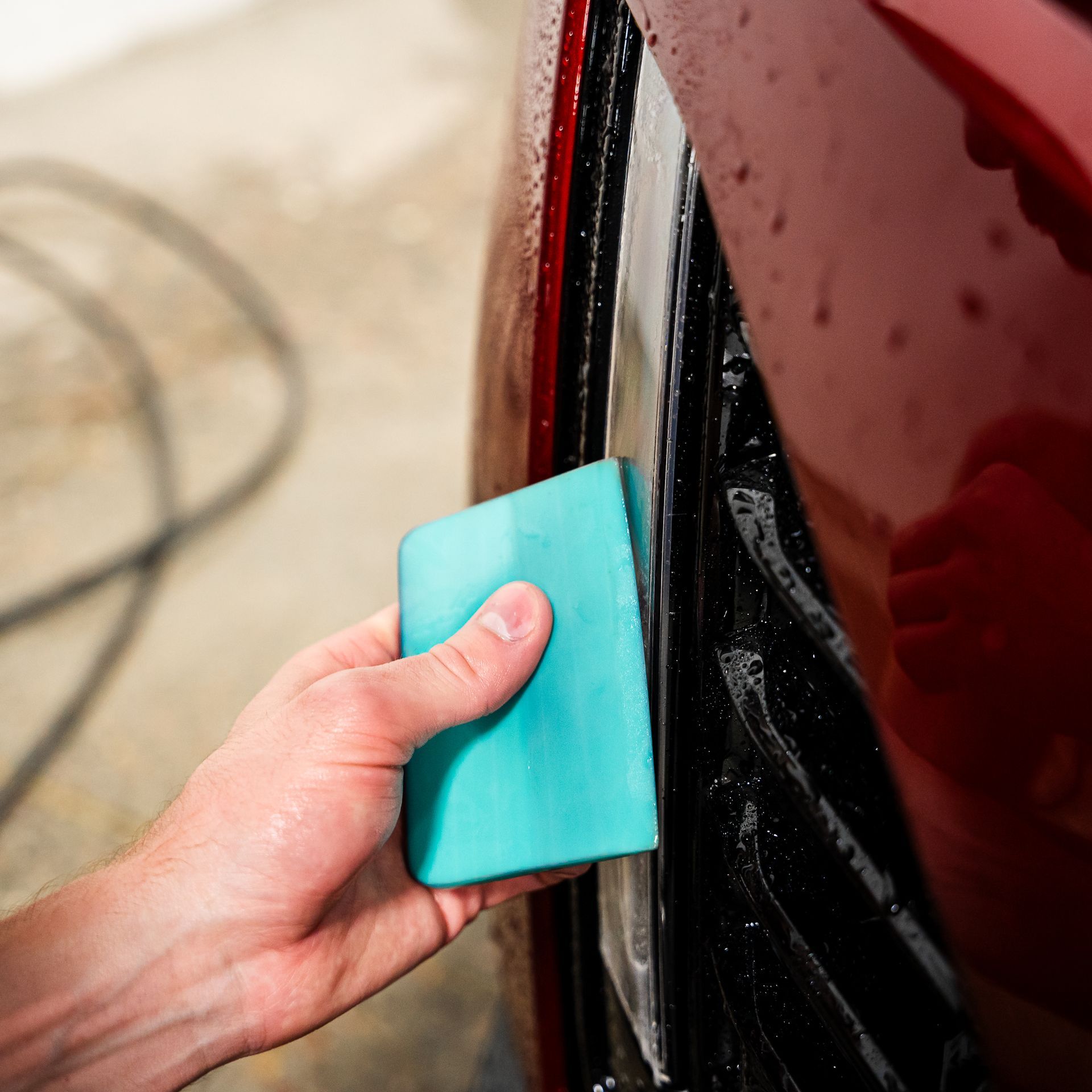 A person is cleaning a red car with a blue sponge