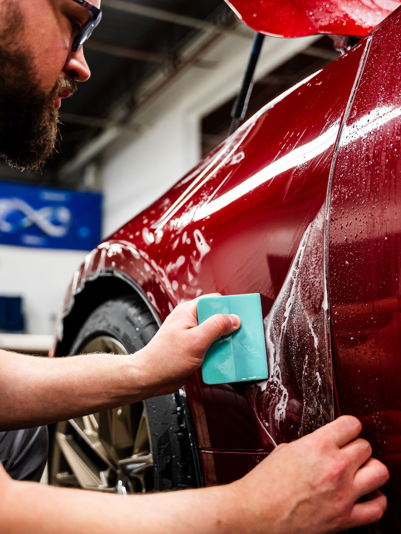 A man is cleaning a red car with a green sponge.