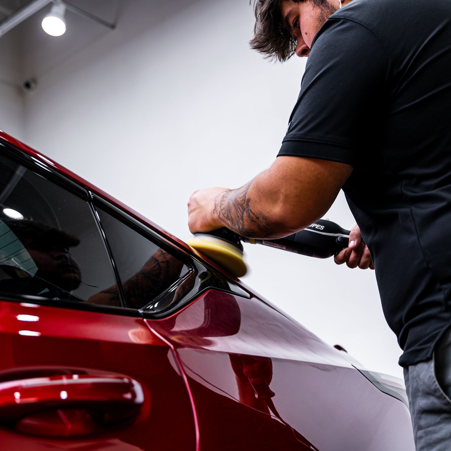 A man is polishing a red car with a polisher.