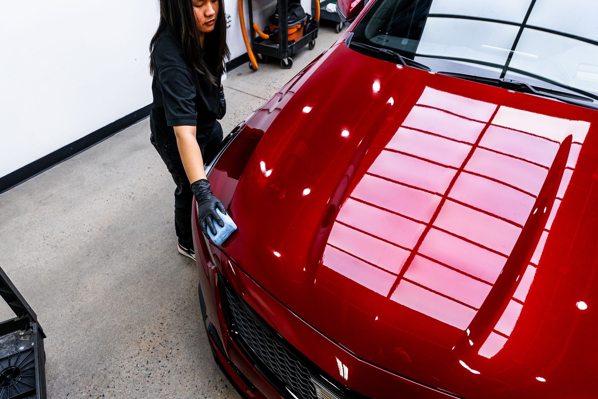 A woman is cleaning the hood of a red car in a garage.