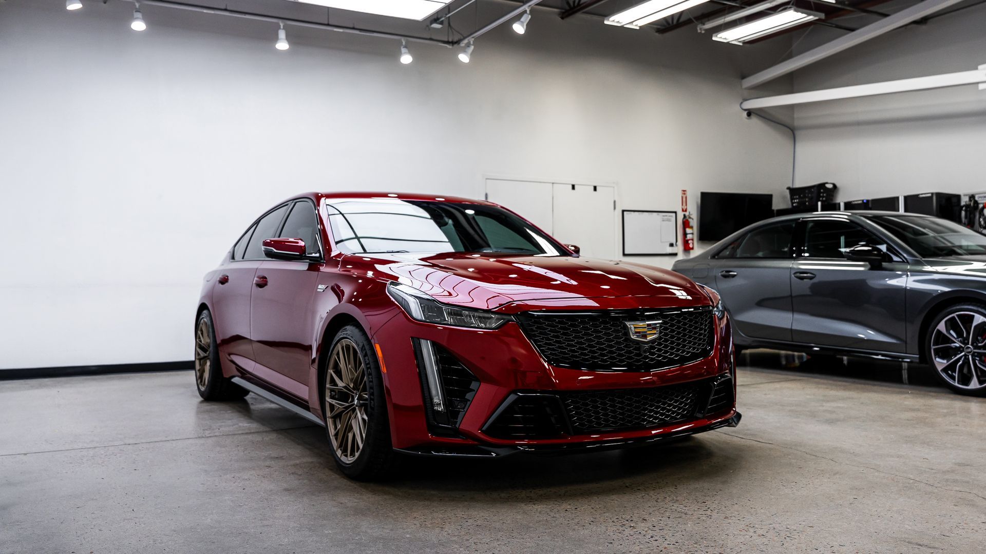 A red cadillac is parked in a garage next to a gray car.