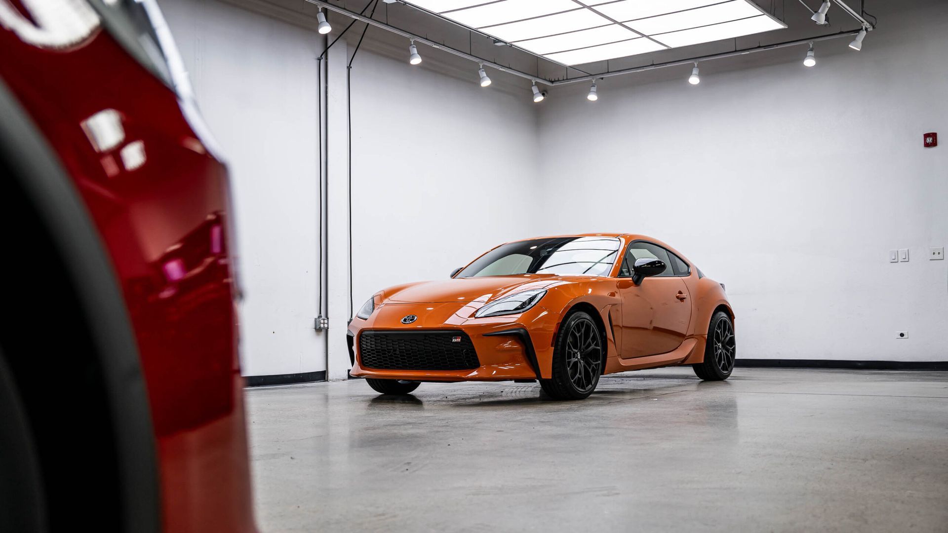 An orange sports car is parked in a garage next to a red car.