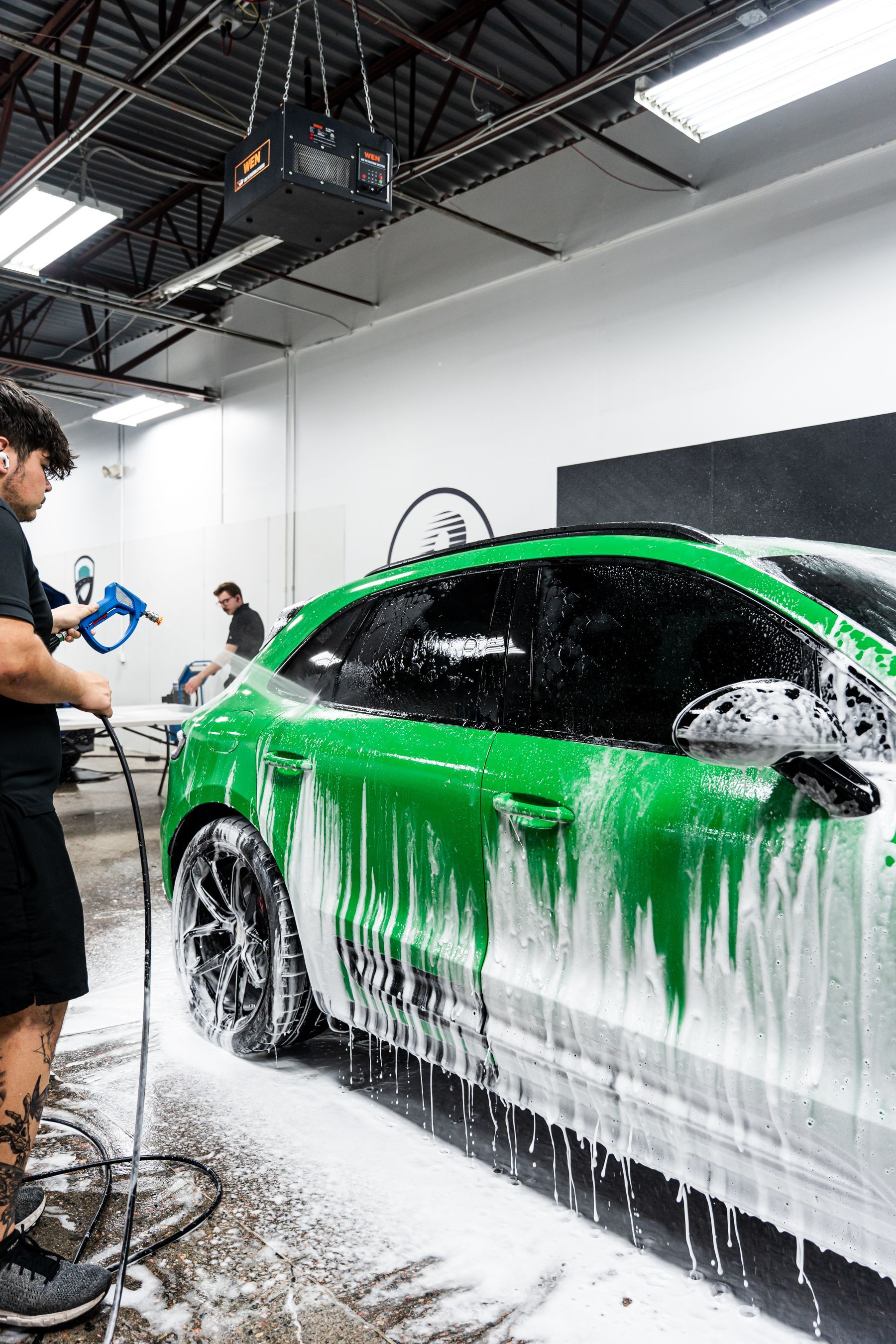 Man washing a bright green car with soapy foam in a garage.