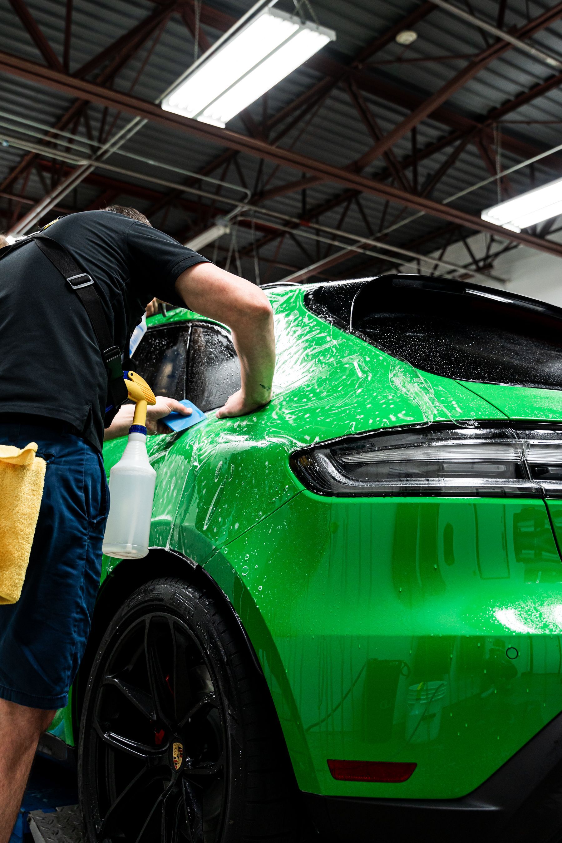 Person washing a vibrant green car, with soapy water, in a garage.