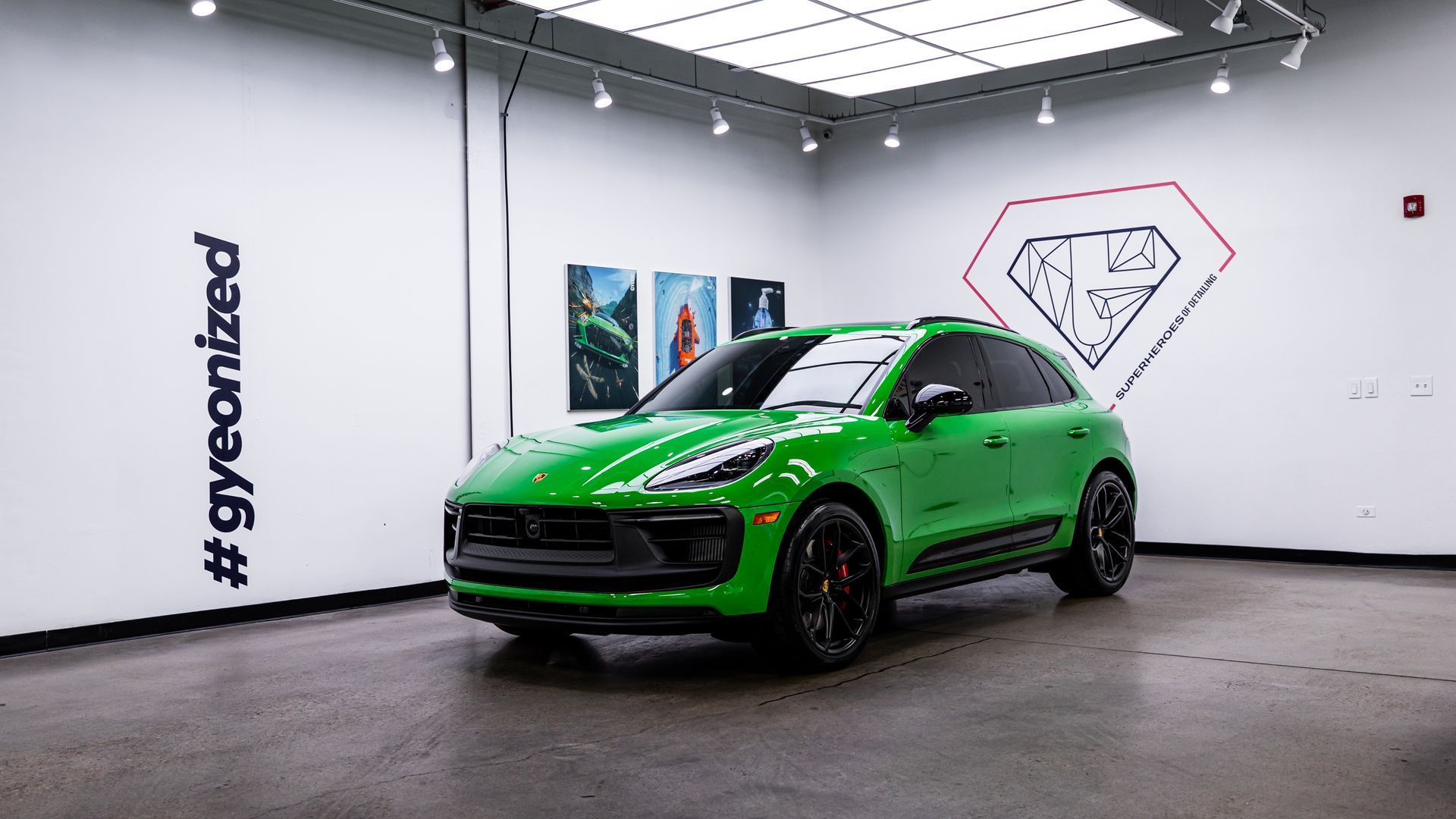 Green Porsche SUV in a well-lit showroom. Black accents, white walls, and a diamond logo visible.
