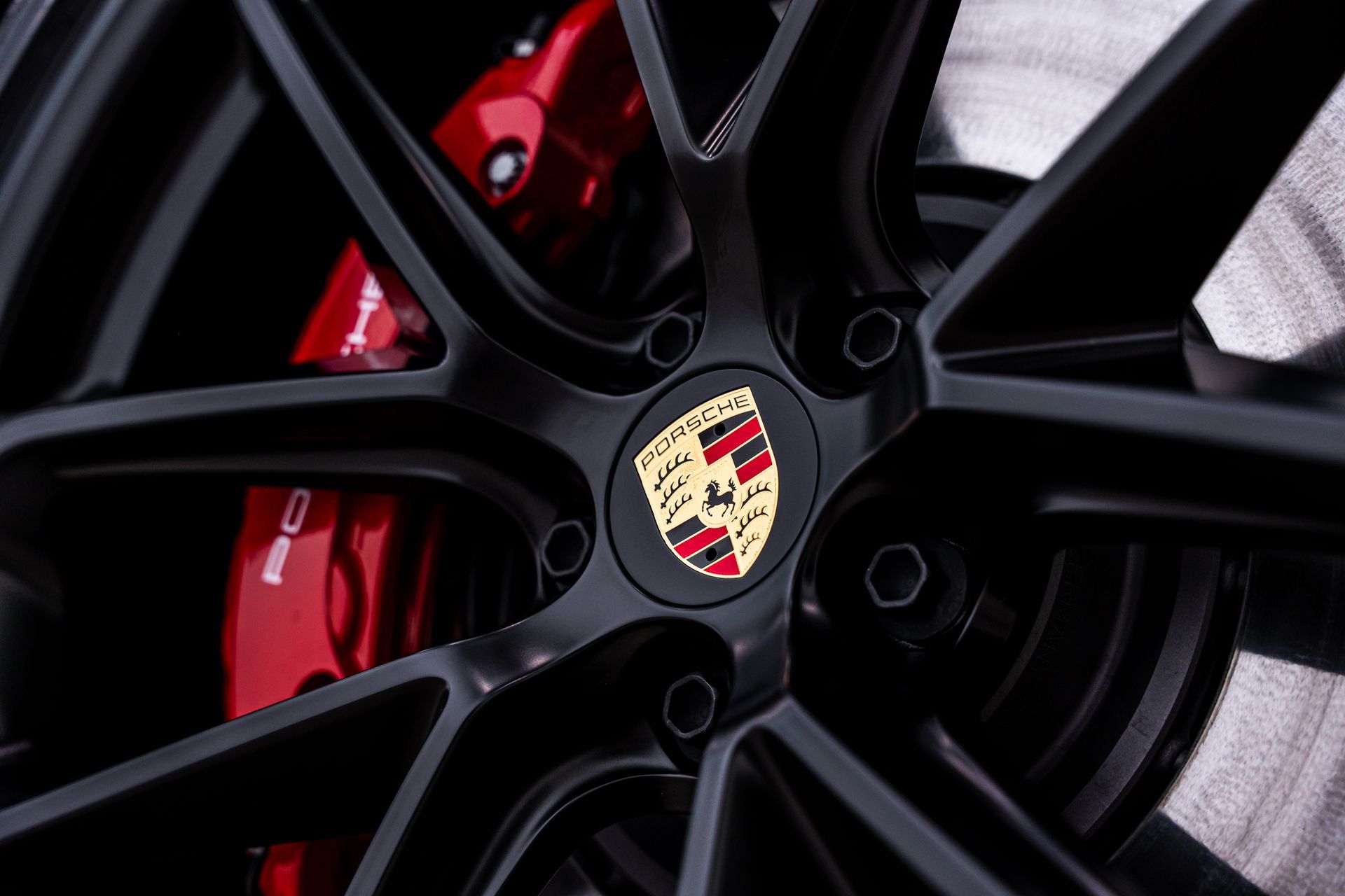 Black Porsche wheel with red brake caliper and gold emblem.