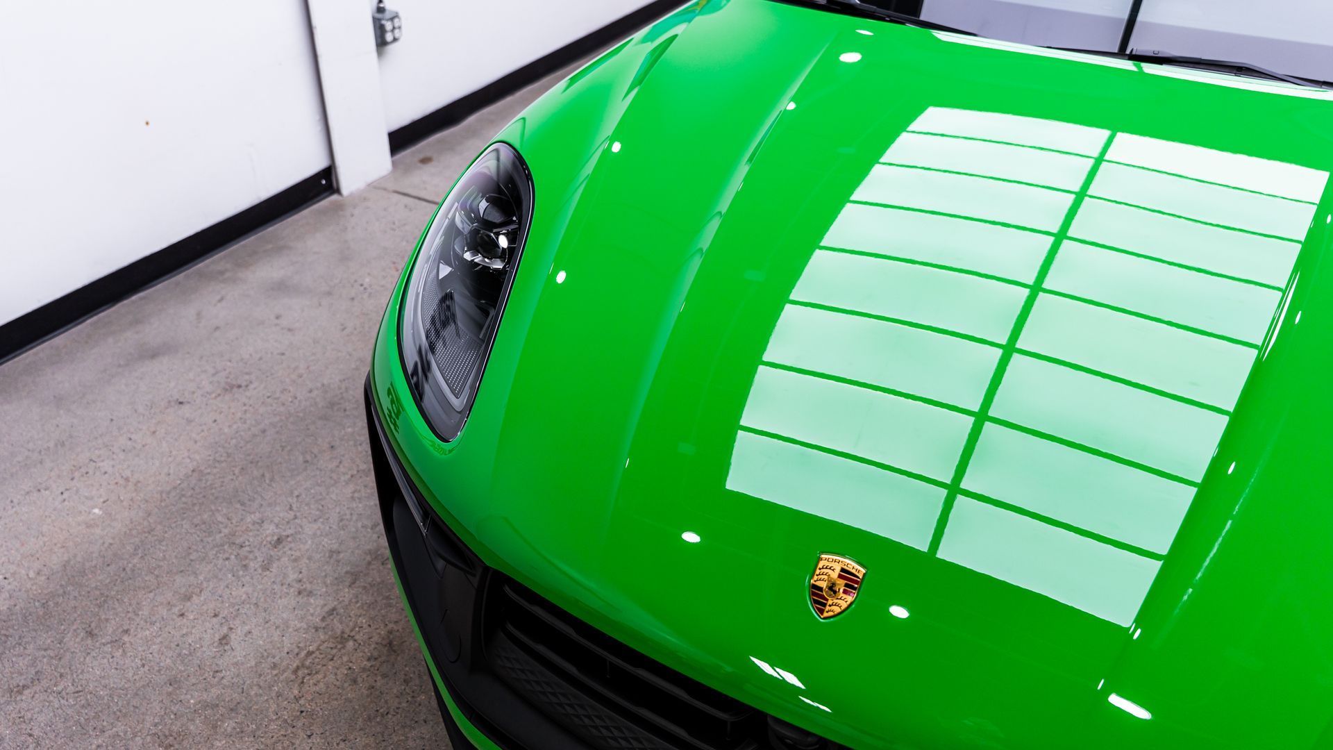 Bright green Porsche car hood with reflection of grid lights in a garage.
