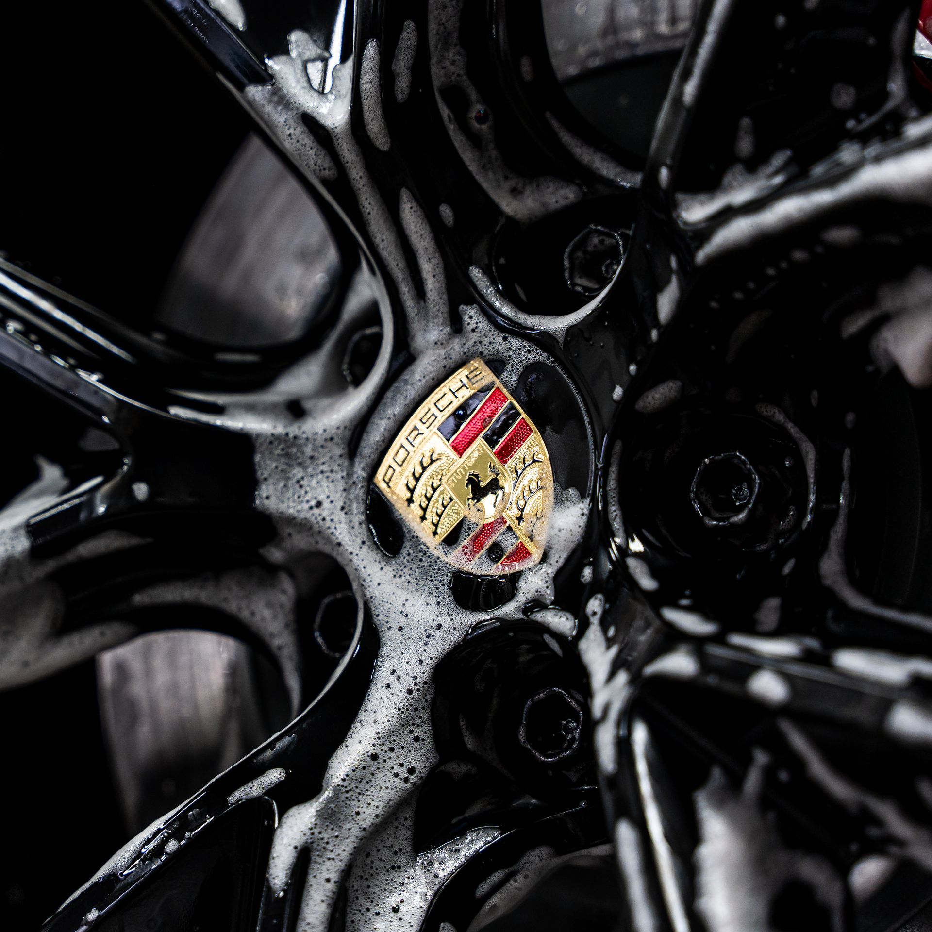 Black Porsche wheel with soapy foam surrounding the logo.