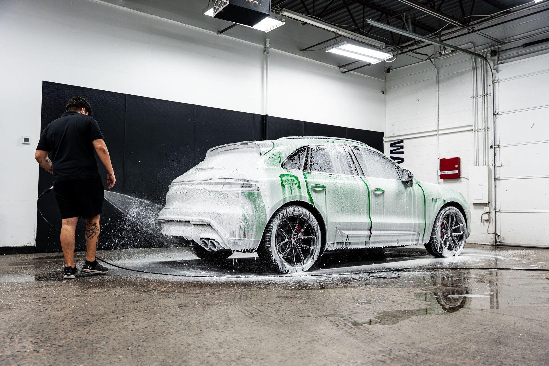 Man washing a green car with foam in a garage.