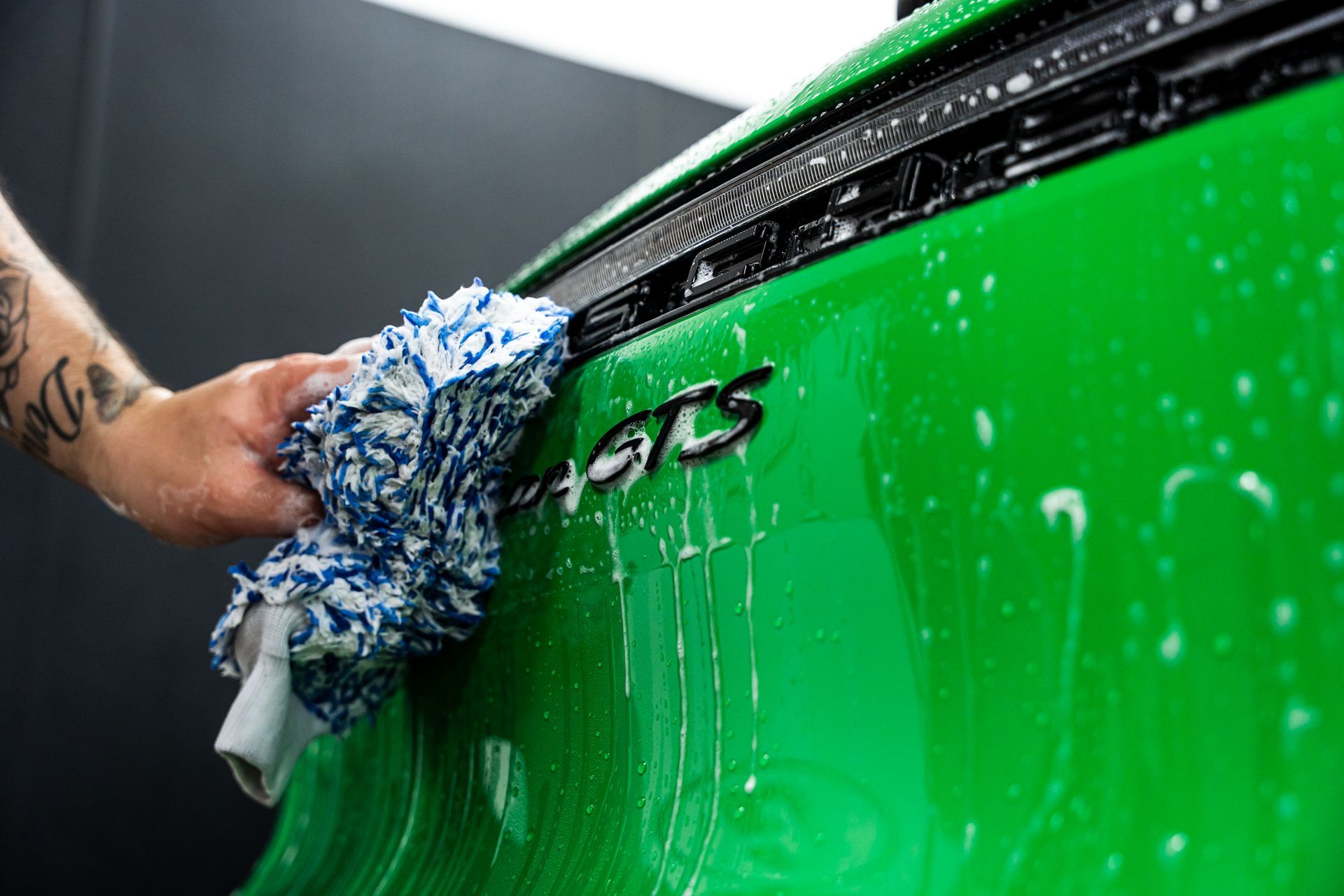 Person washing a green car with a blue and white wash mitt. 