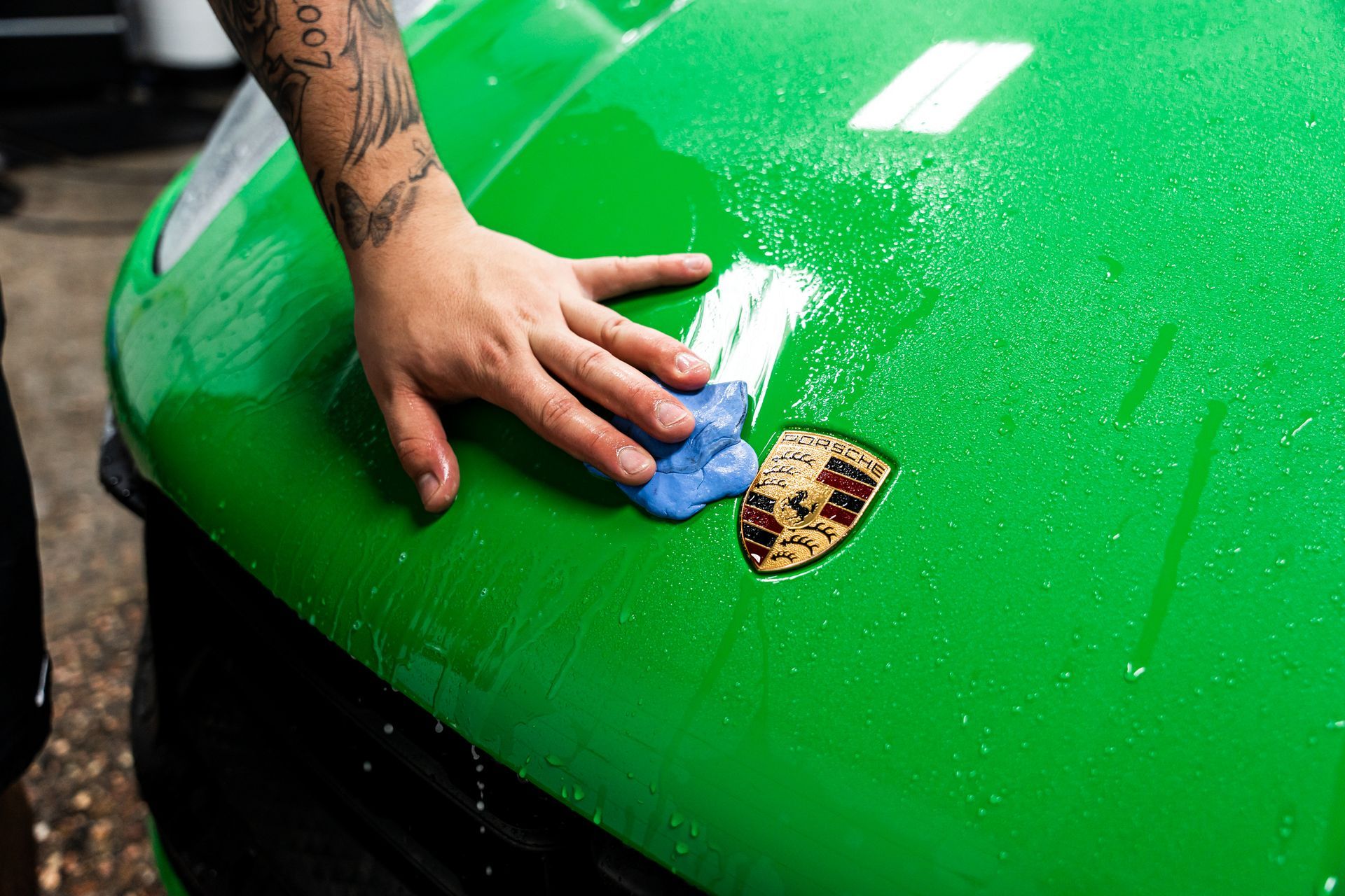 Person clay barring a green Porsche hood with water and logo visible.