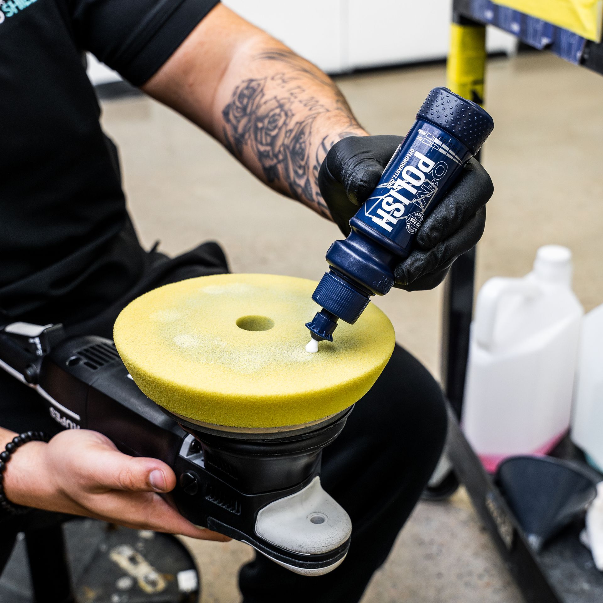 Person applying polish to a yellow buffing pad with a polisher in a shop.