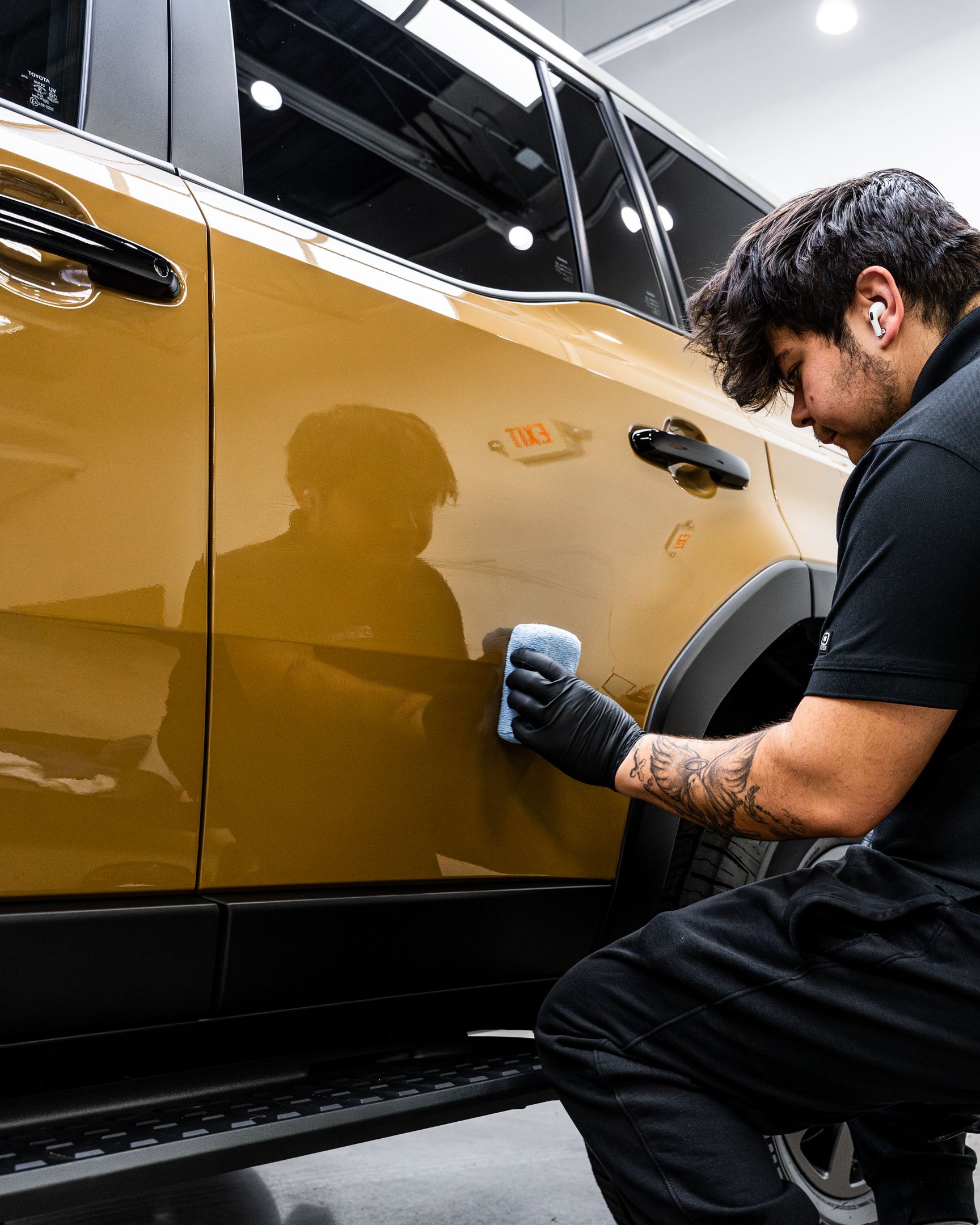 Person in black clothing applying car wax to a gold SUV door.
