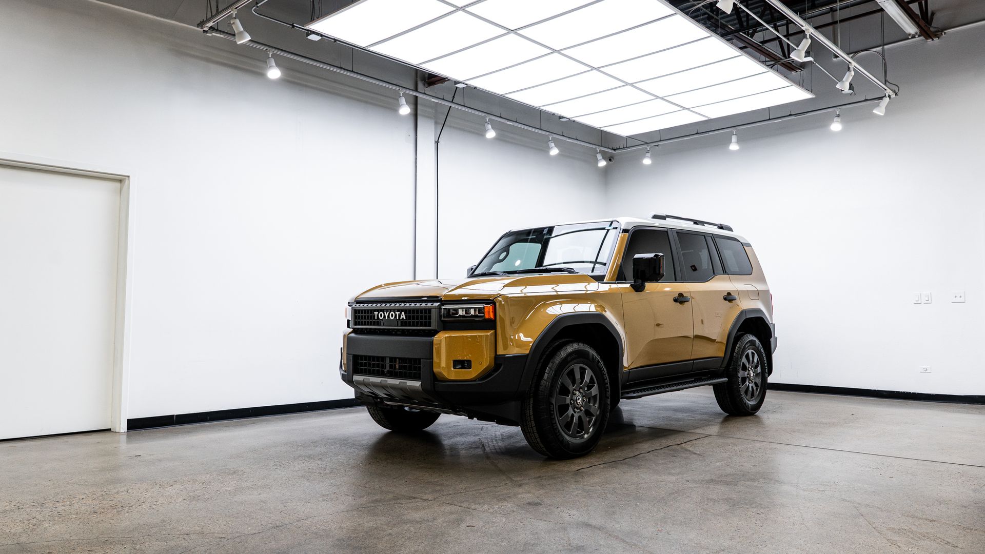 Gold SUV parked in a bright white studio with concrete flooring and overhead lighting.