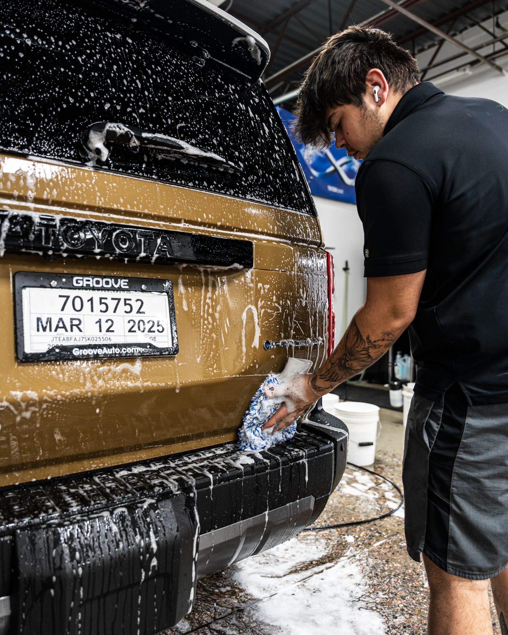 Man washing a gold SUV, covered in soap. License plate visible.