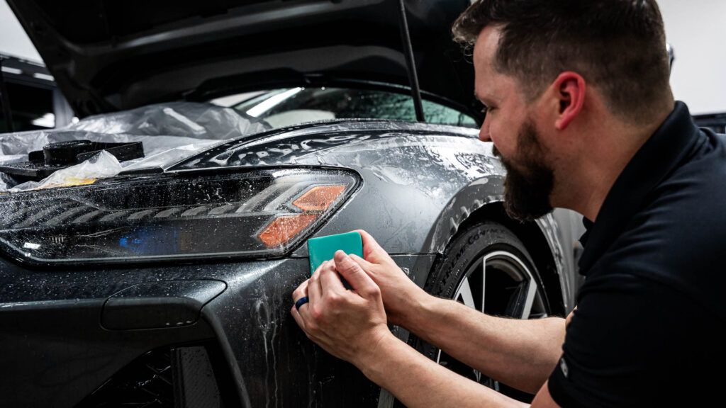 A man is applying protective film to the front of a car.