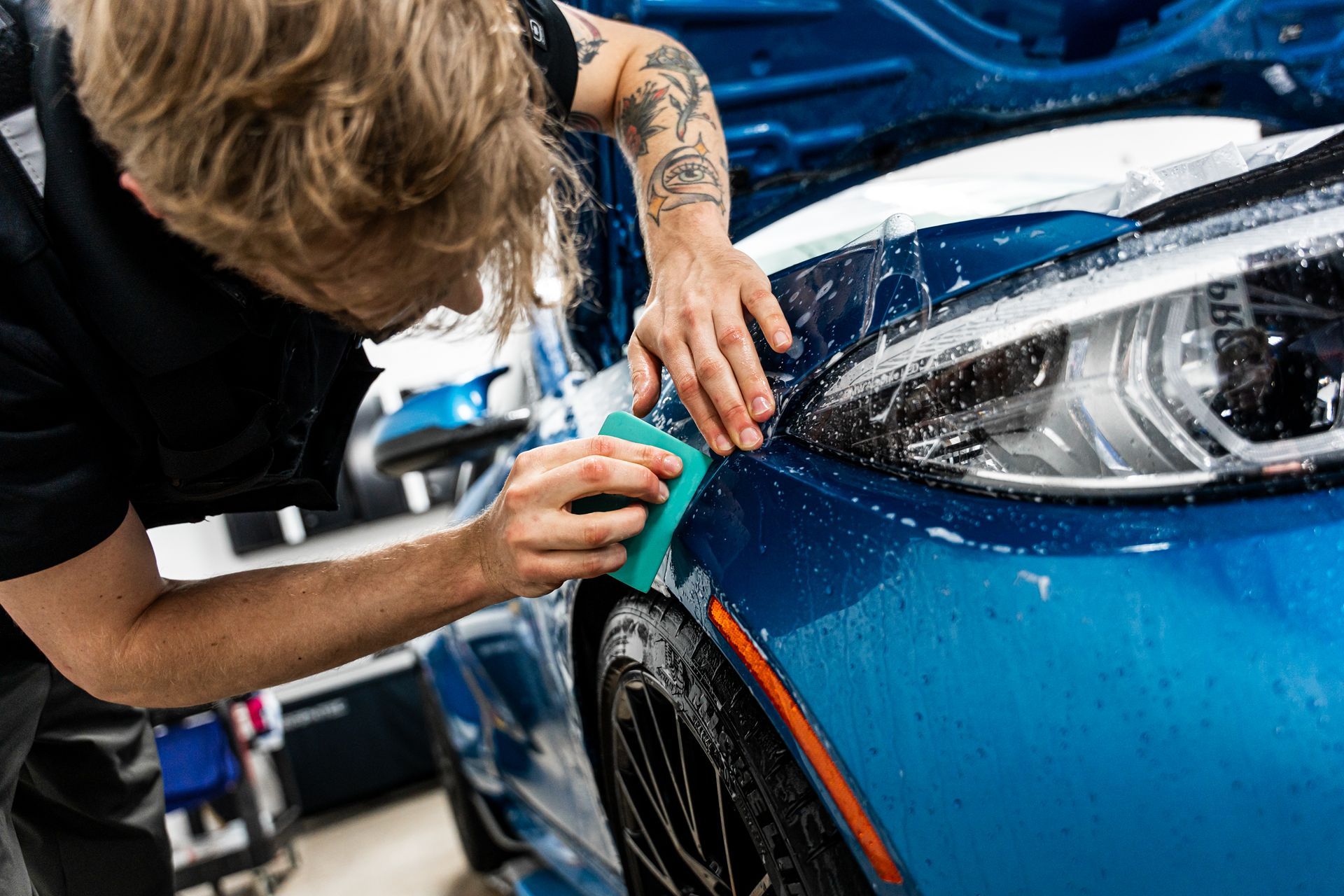 Man washes a blue car with a sponge, outdoors.