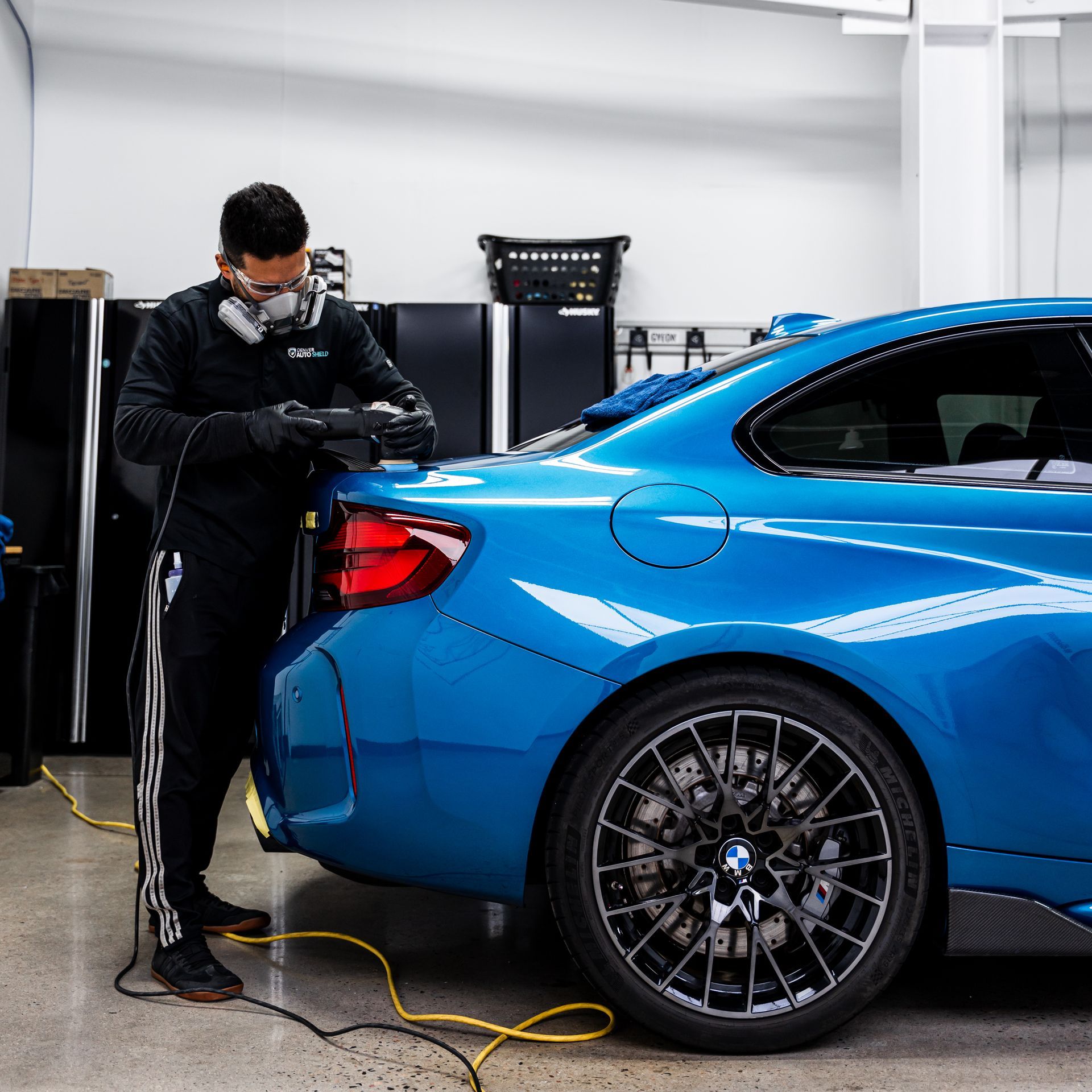 Man polishing a blue BMW car in a garage, wearing a respirator and gloves.