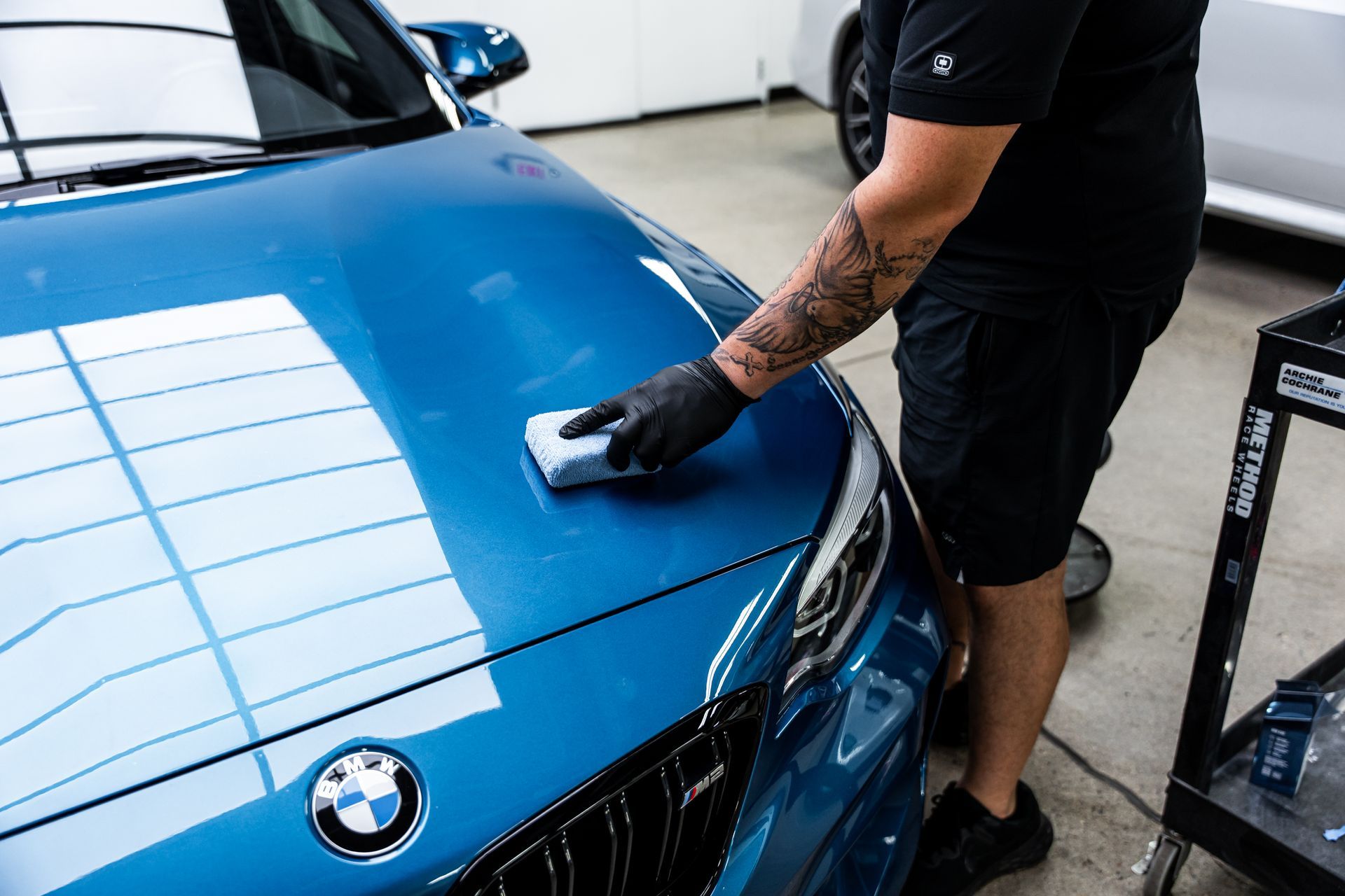 Person applying a ceramic coating to the hood of a blue BMW car.