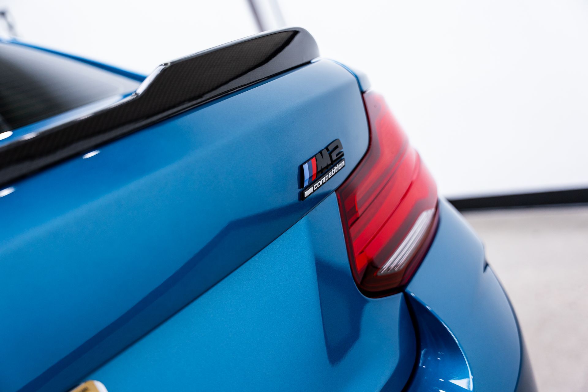 Blue BMW M2 car with a carbon fiber spoiler and M2 badge.