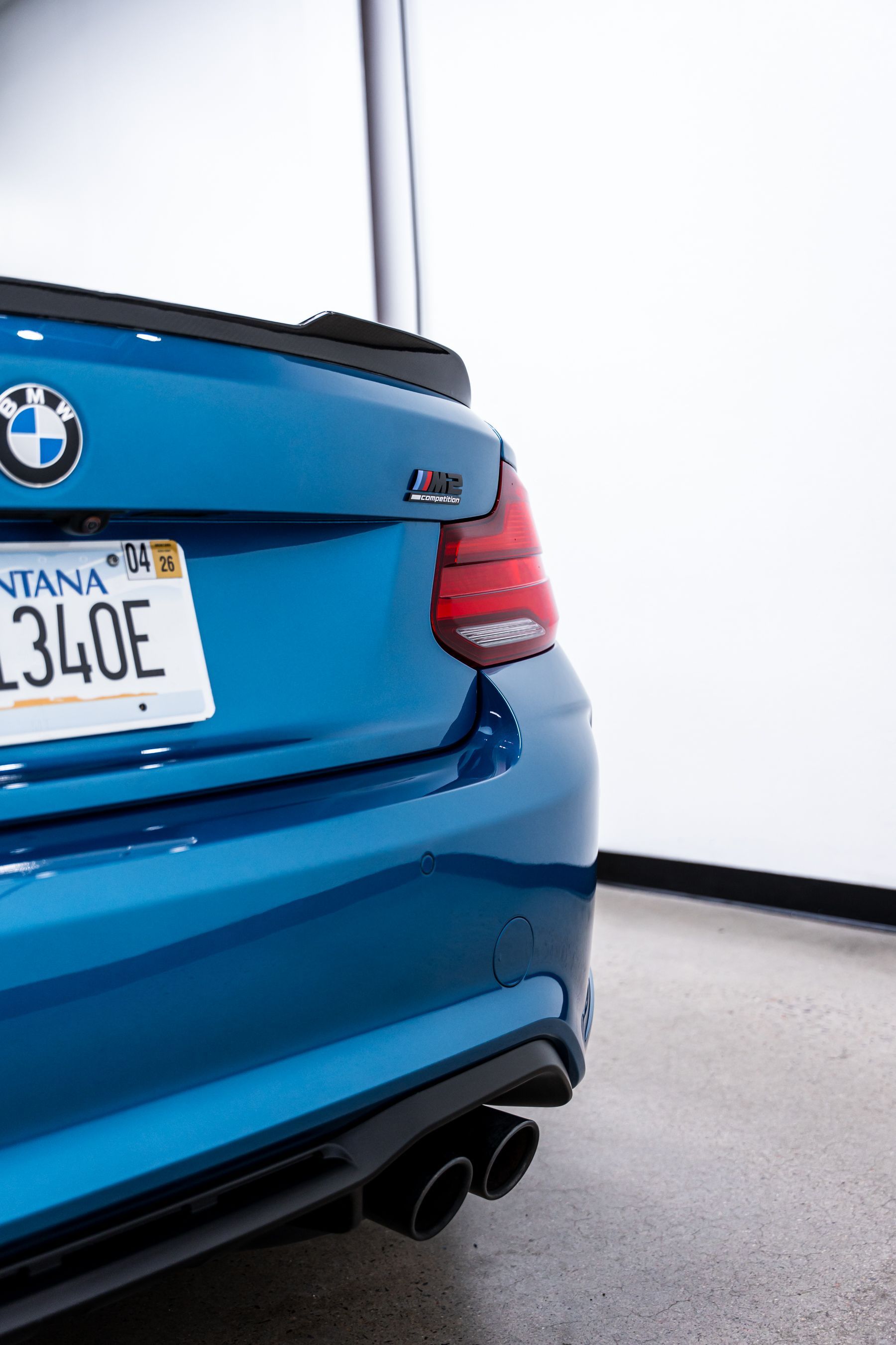 Blue BMW M2 rear corner, showing taillight, exhaust, and Montana license plate.