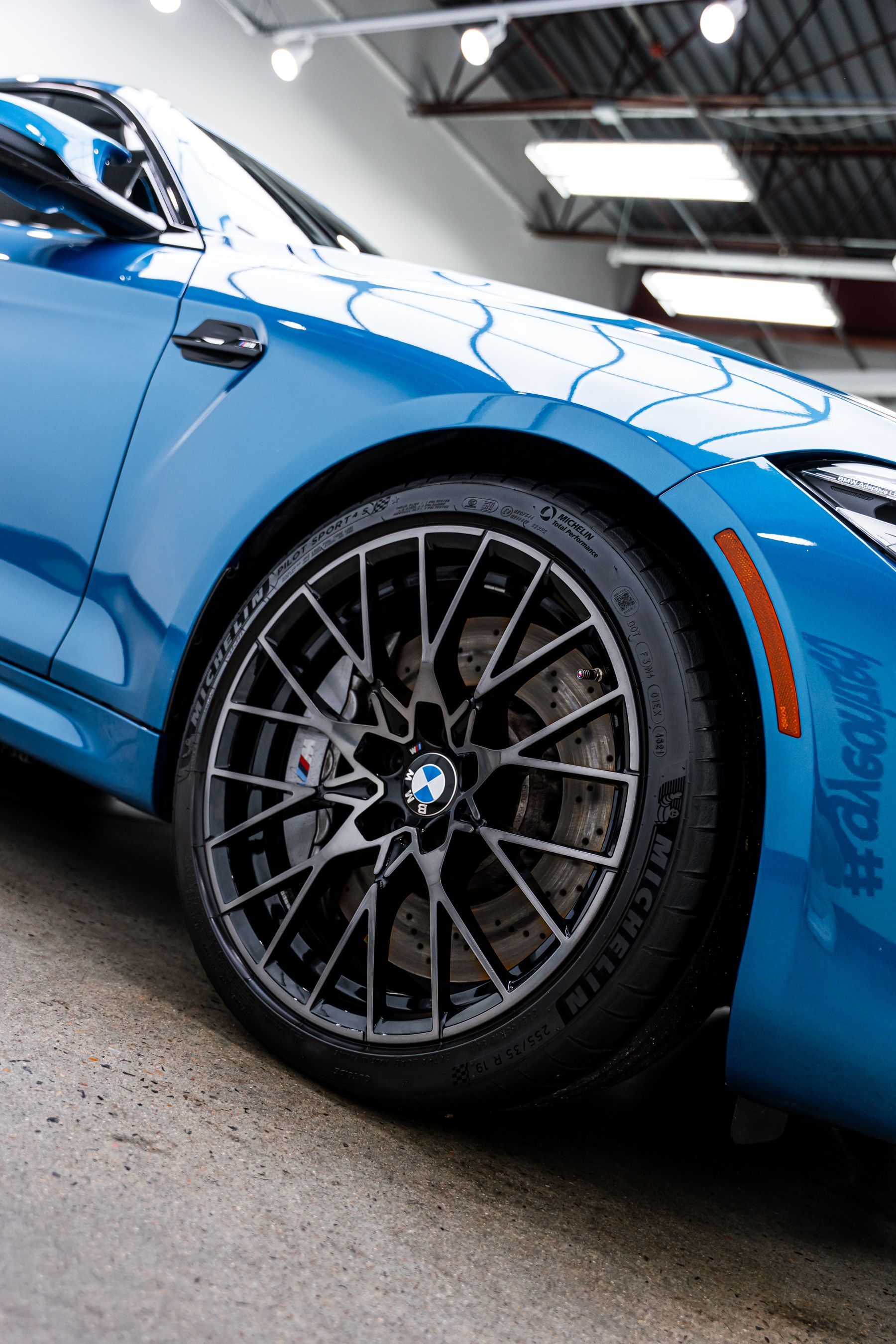 Blue BMW car, close-up of front wheel, dark gray rims, and brake disc.