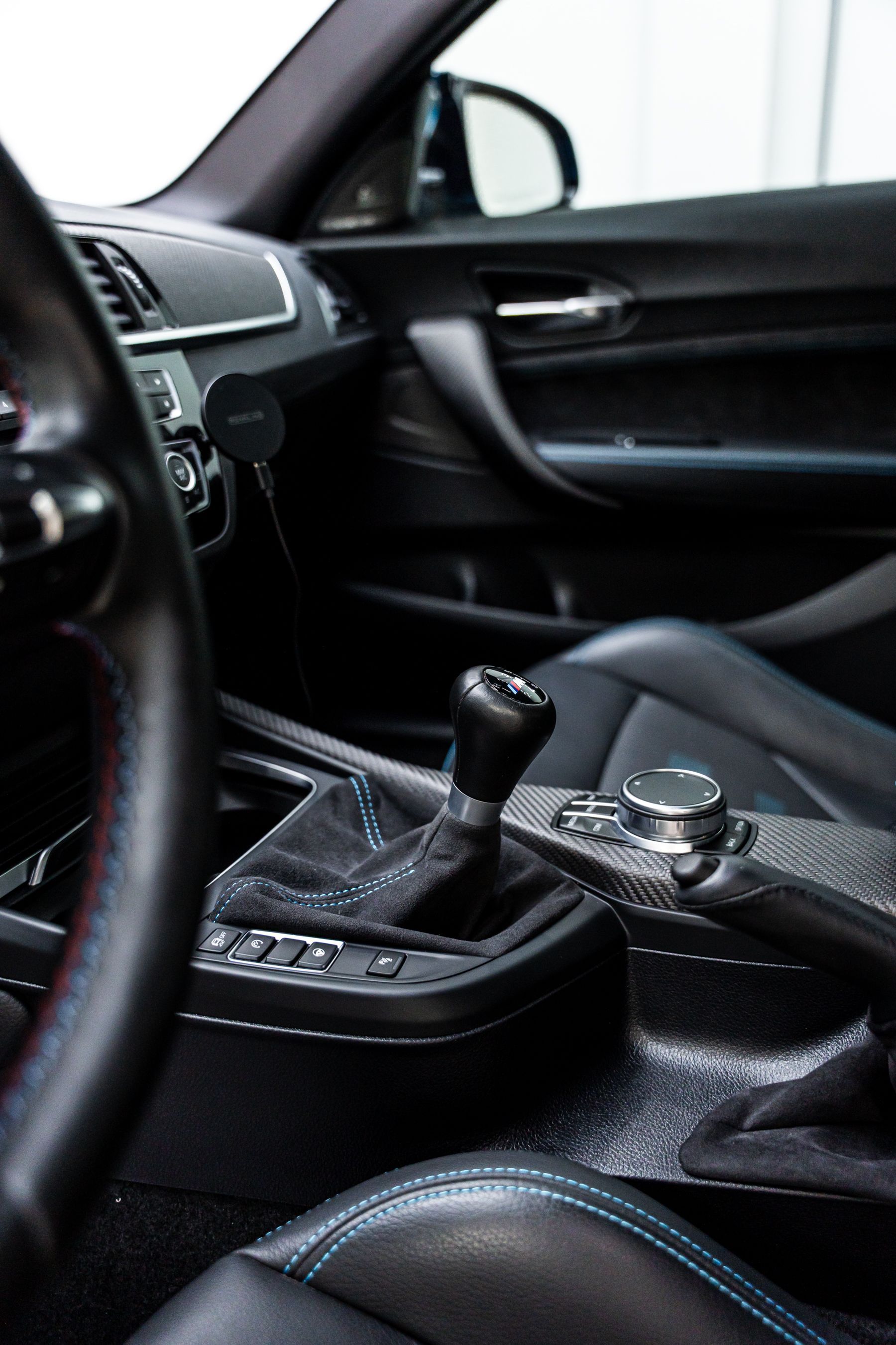 Interior view of a black car's gear shift, leather seats with blue stitching, and dark dashboard.