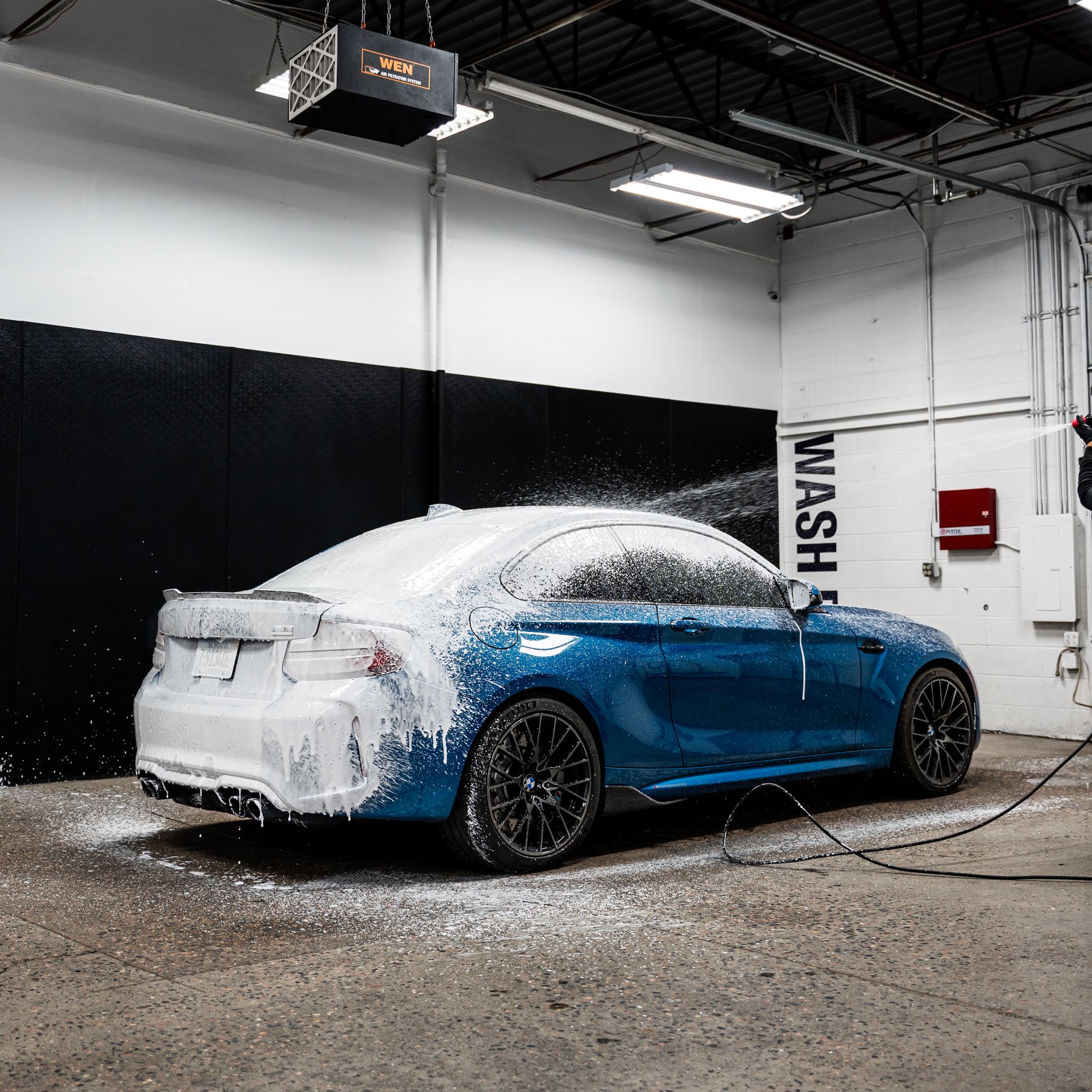 A blue car covered in white foam being washed at a car wash facility.