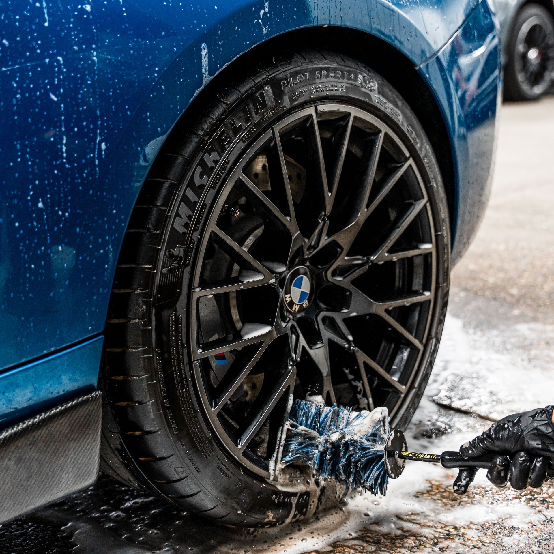 Blue car wheel being washed with a brush, close-up view.