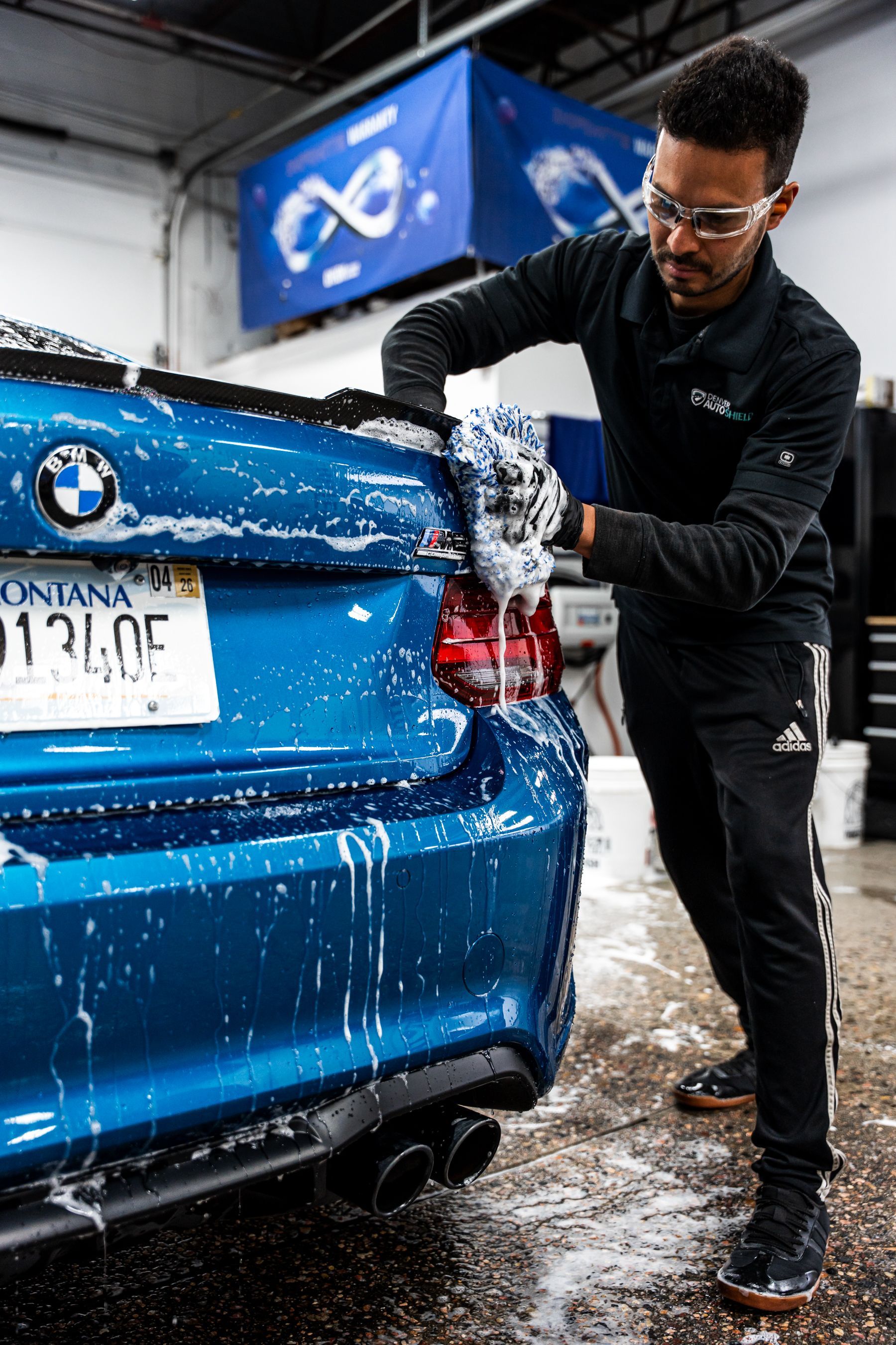 Man washing a blue BMW car, covered in soap, in a car wash bay.