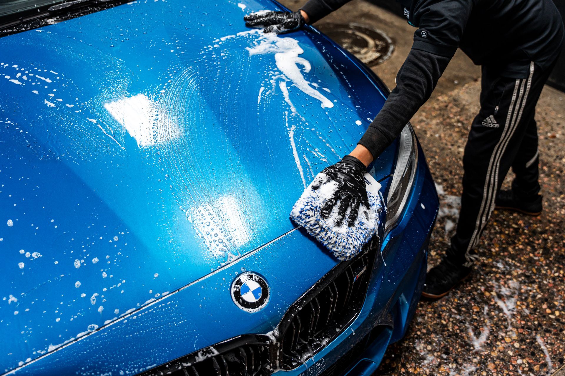 Person washing a blue BMW car with a sponge.