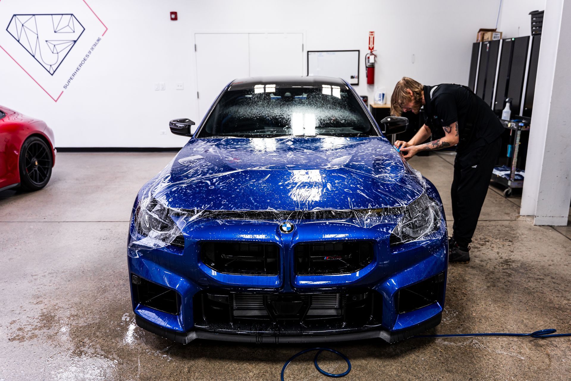 A person washing a blue car in a garage with soapy water.