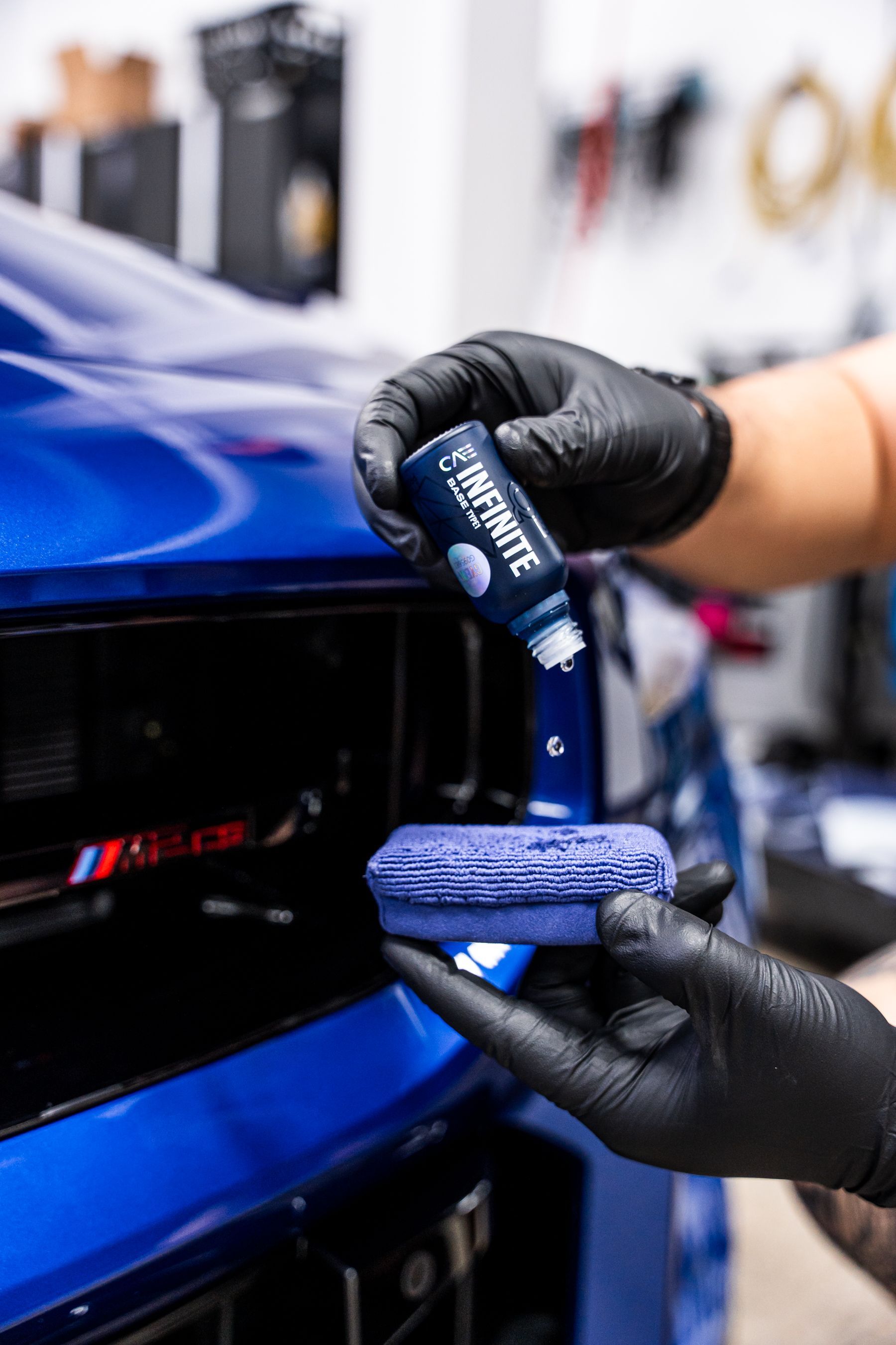 Person applying car sealant to a blue car grill with a black-gloved hand.