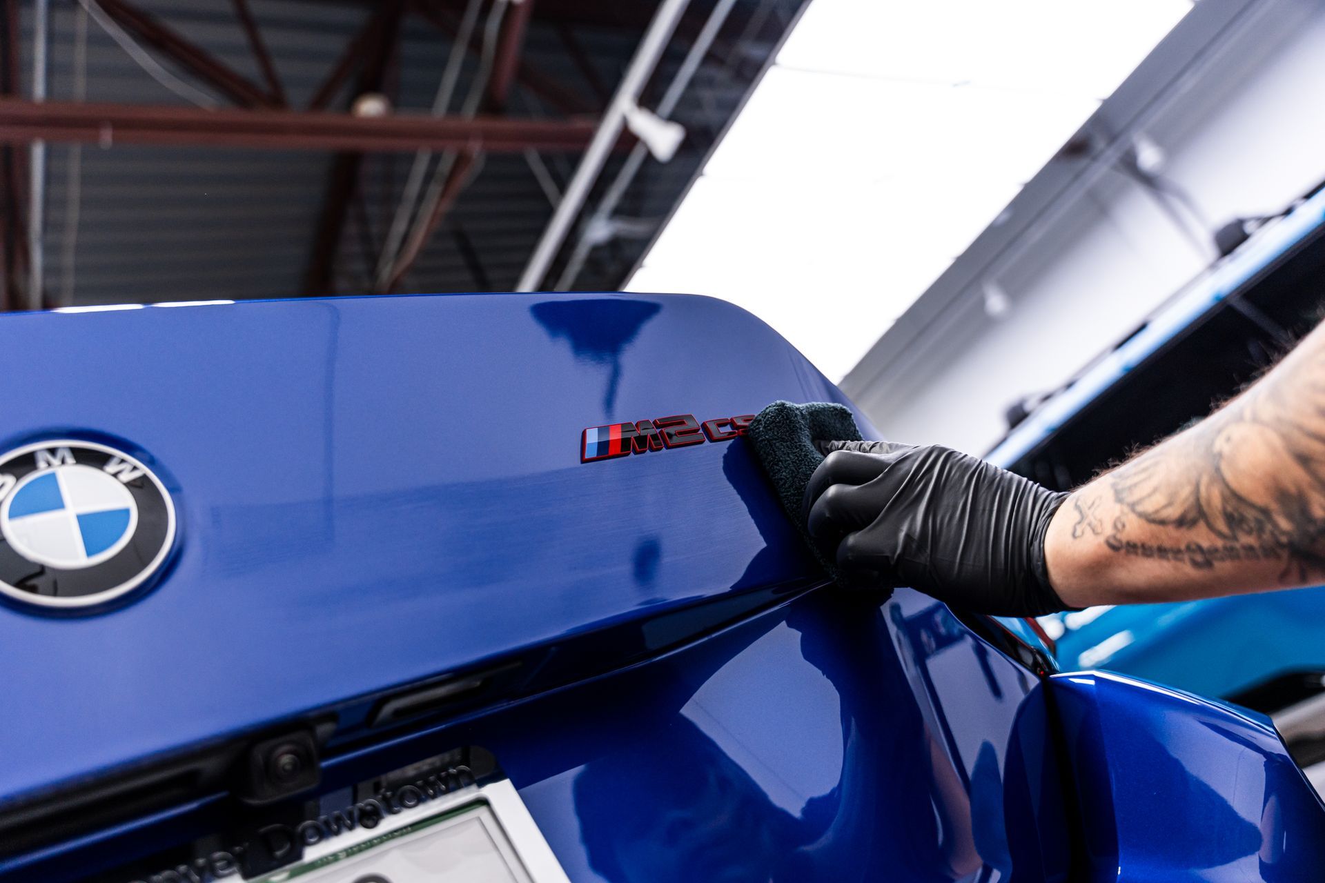 Person in black gloves detailing a blue BMW trunk, applying product with a sponge.