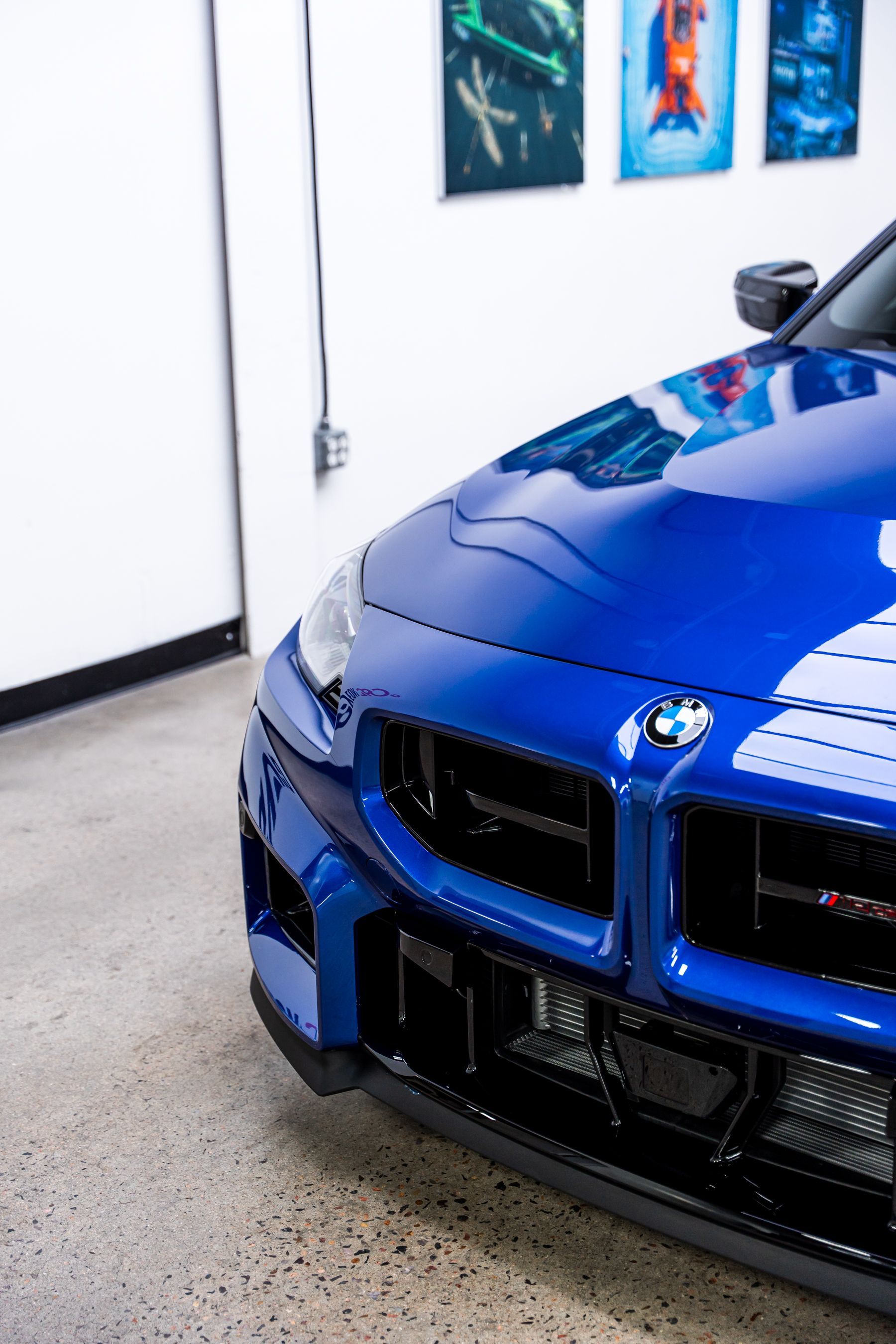 Blue BMW sports car front, parked indoors, near a white wall.