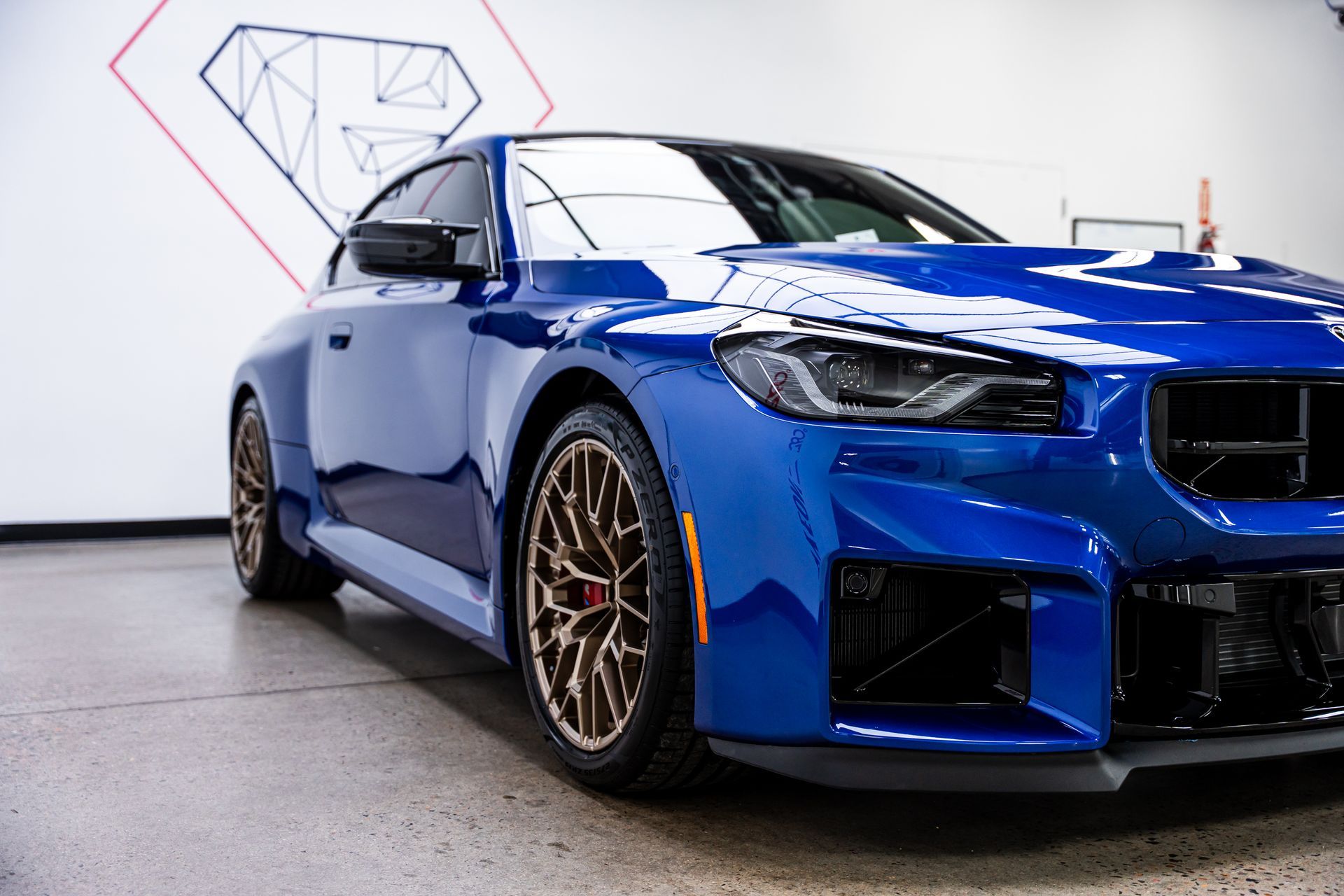 Blue BMW sports car parked indoors, bronze wheels, black front grill, and orange side marker lights.