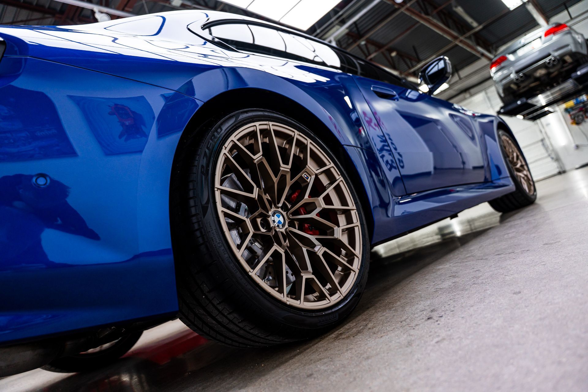 Blue sports car with bronze wheels in a garage, another car on a lift in background.